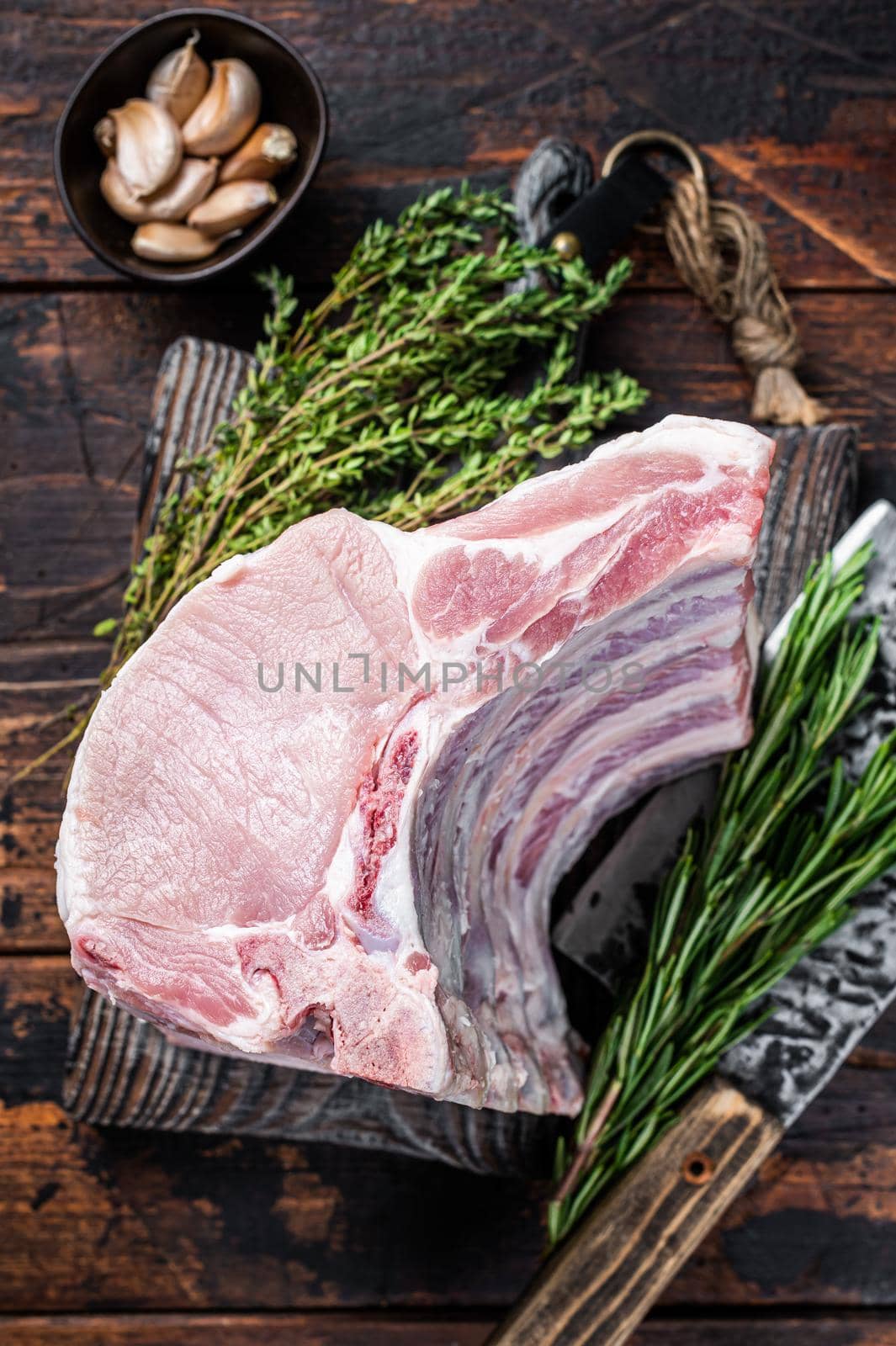 Raw rack of pork loin chops with ribs on a butcher board with meat cleaver. Dark wooden background. Top view.