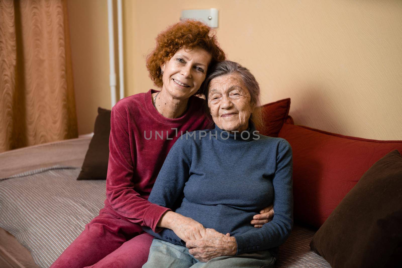 Adult daughter takes care of elderly mother suffering from dementia, old woman ninety years age gray hair and wrinkles on face and sweet kind smile, family idyll caring for elderly, hug each other by Tomashevska