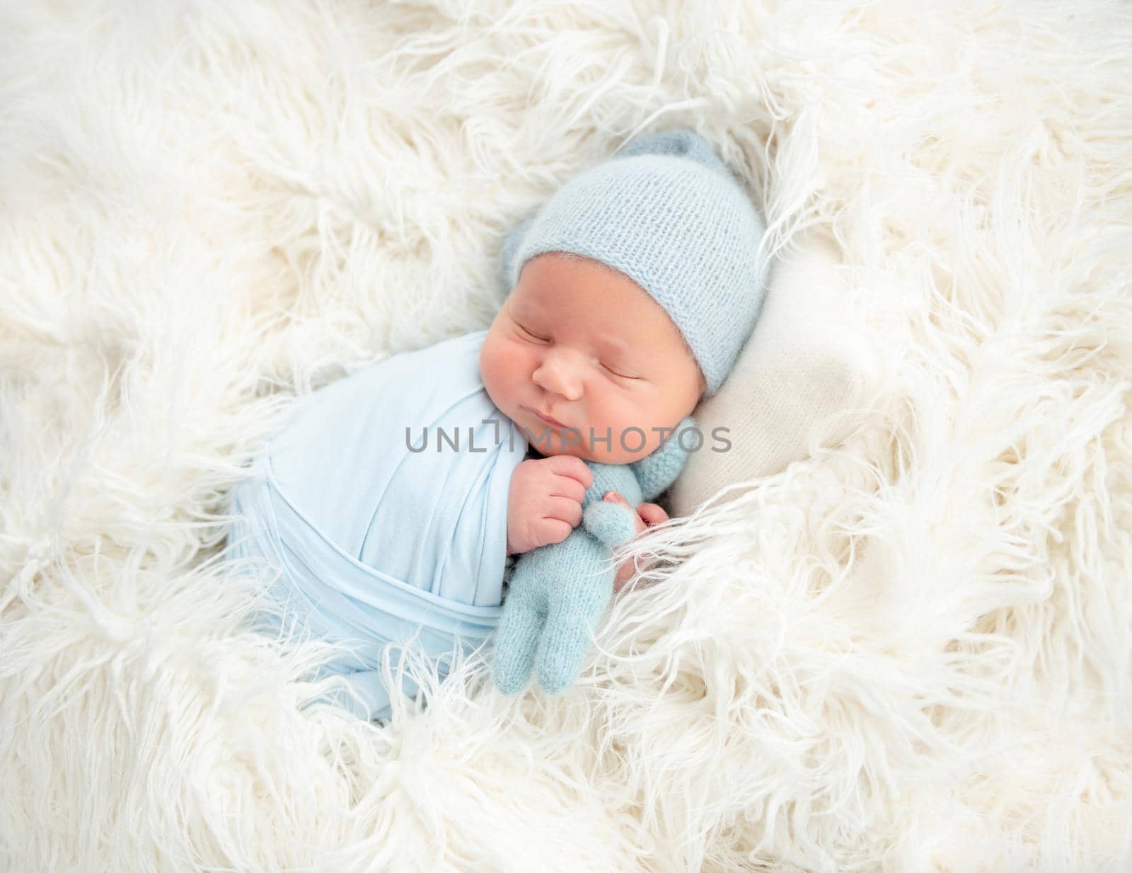 Sleeping newborn in knitted hat hugging toy