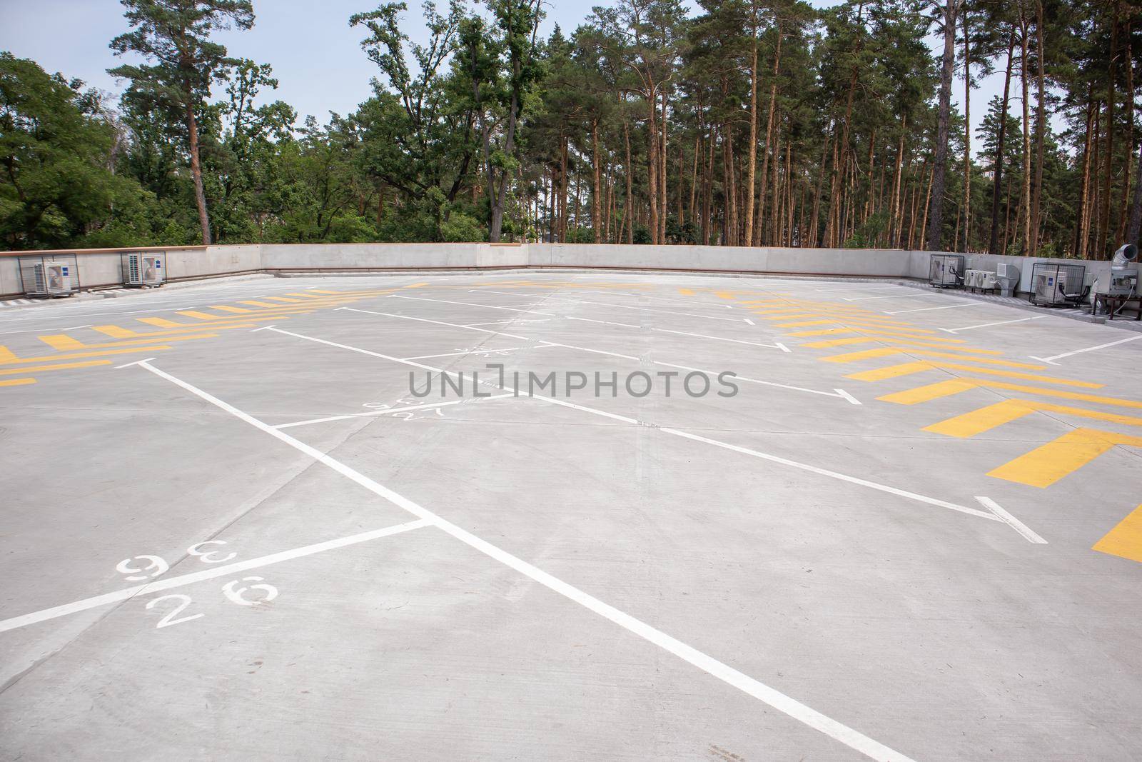 Empty rooftop parking. Directional traffic arrows and parking spots are marked with white and yellow paint on the asphalt. Parking space without cars with city skyline and park with trees