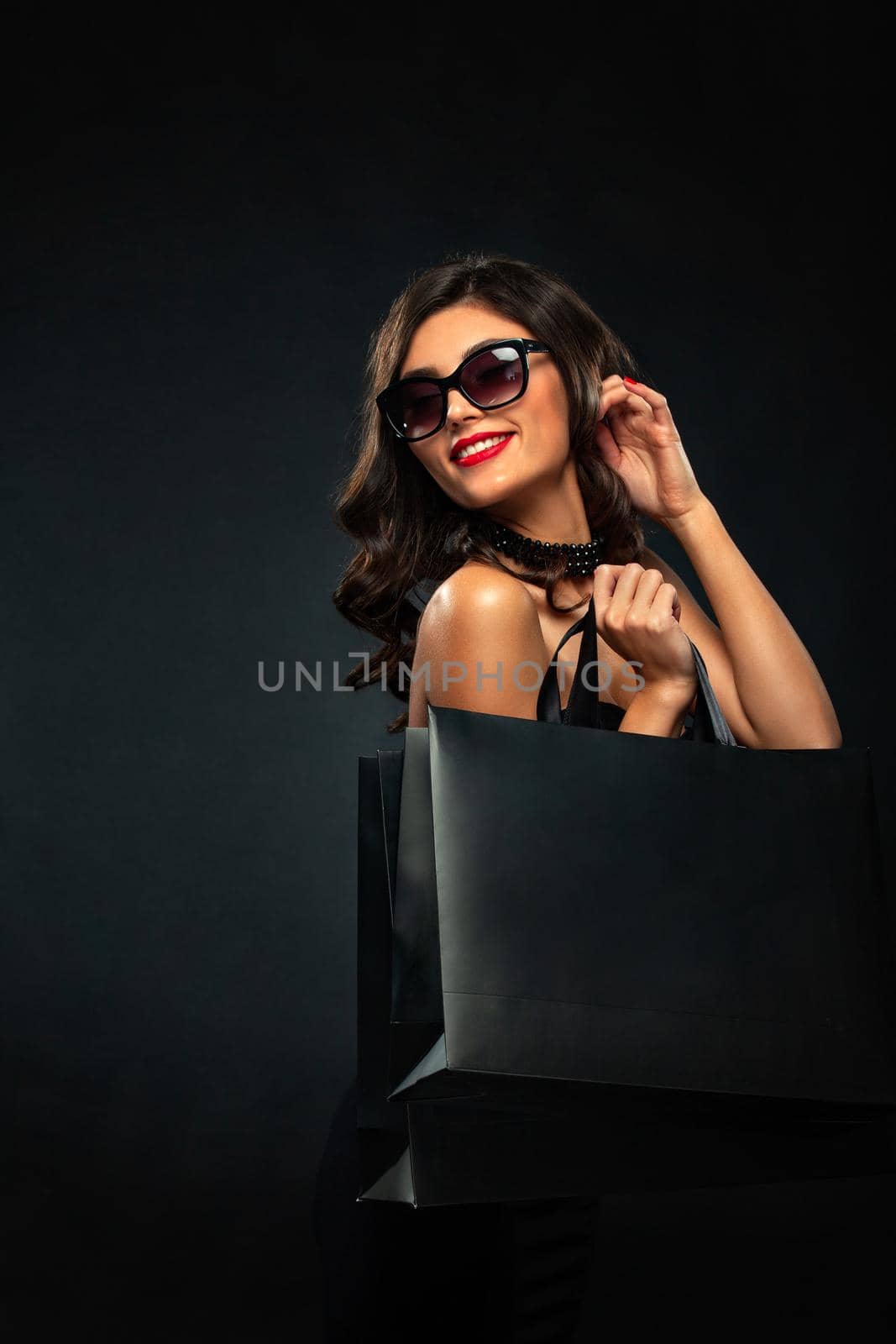 Beautiful young woman make shopping in black friday holiday. Girl with black bag on dark background.