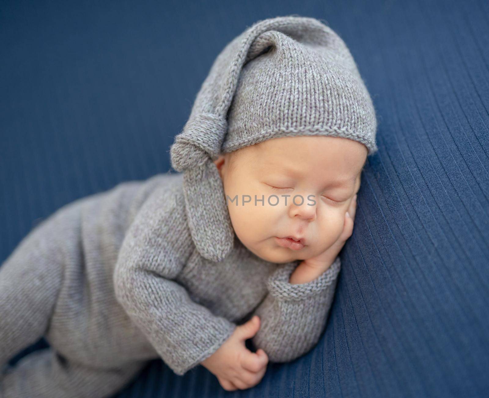 Sweet newborn in knitted suit resting on side with hand under head