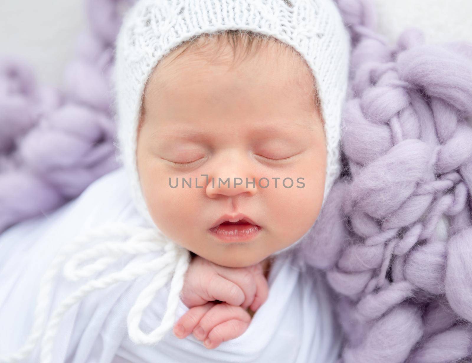 Charming newborn in white knitted hat sleeping close up