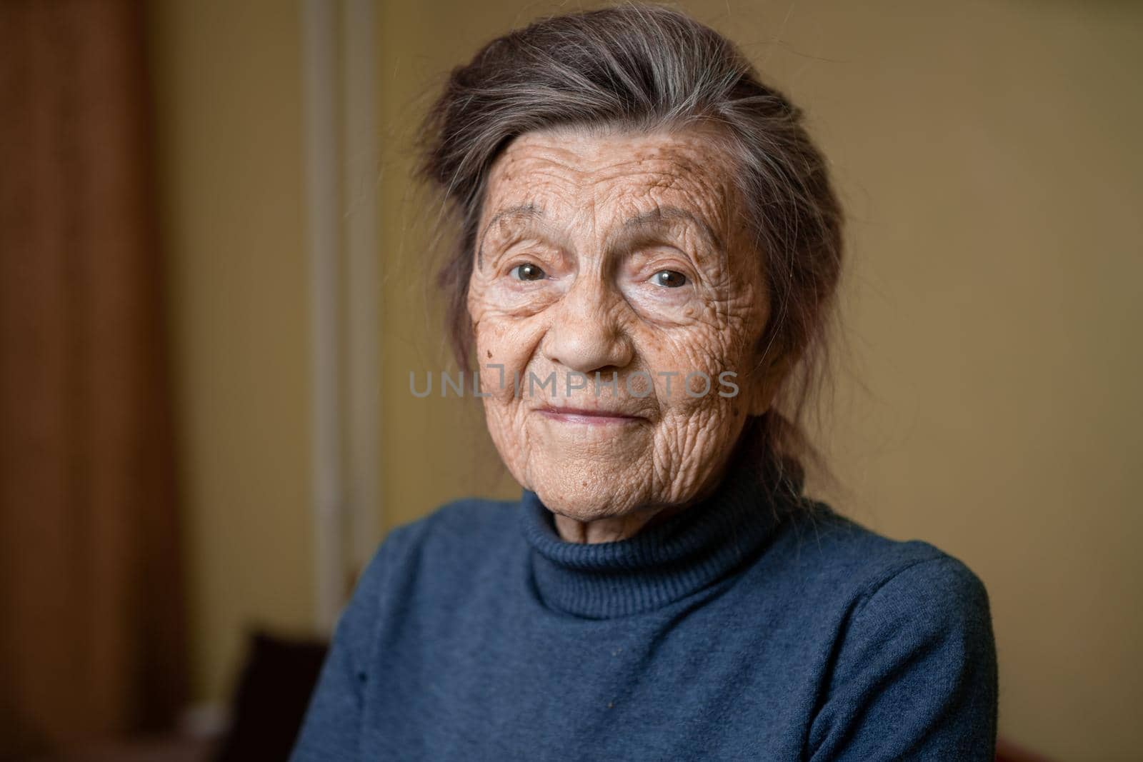 Older cute woman of ninety years old Caucasian with gray hair and wrinkled face looks at camera, cute kind look and smiles.Mature grandmother retired long-liver, theme emotion and mood of old people.