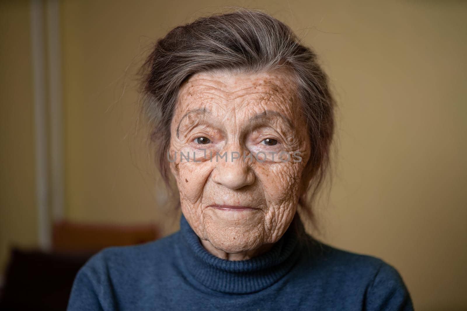 Elderly Caucasian senior grandmother ninety years old looks attentively and smiles, feels happy, large portrait, face with deep wrinkles, gray hair. Theme pensioners, old people and long-lived woman.