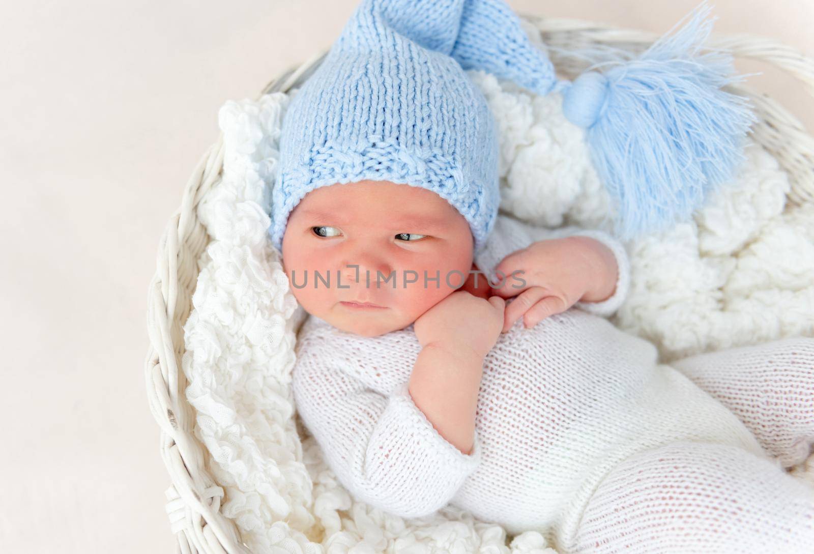 Cute newborn in knitted suit and hat lying in white basket