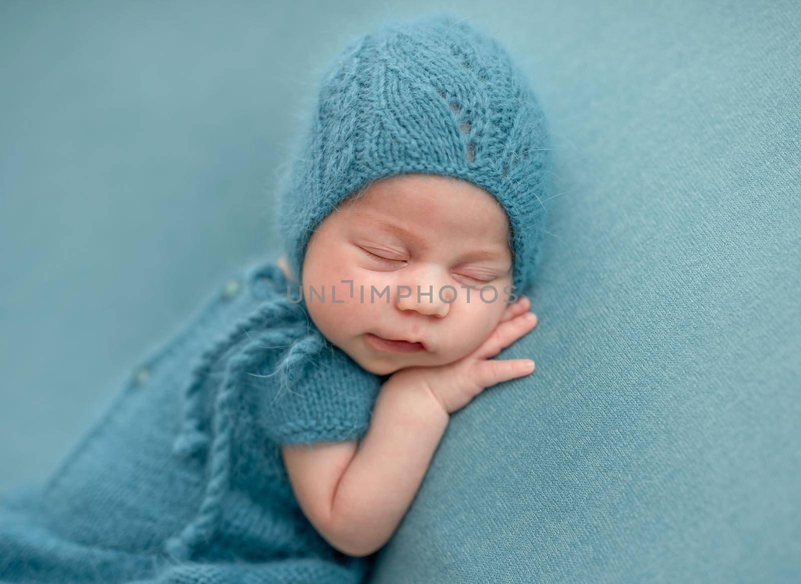 Cute newborn in knitted suit sleeping on blue background