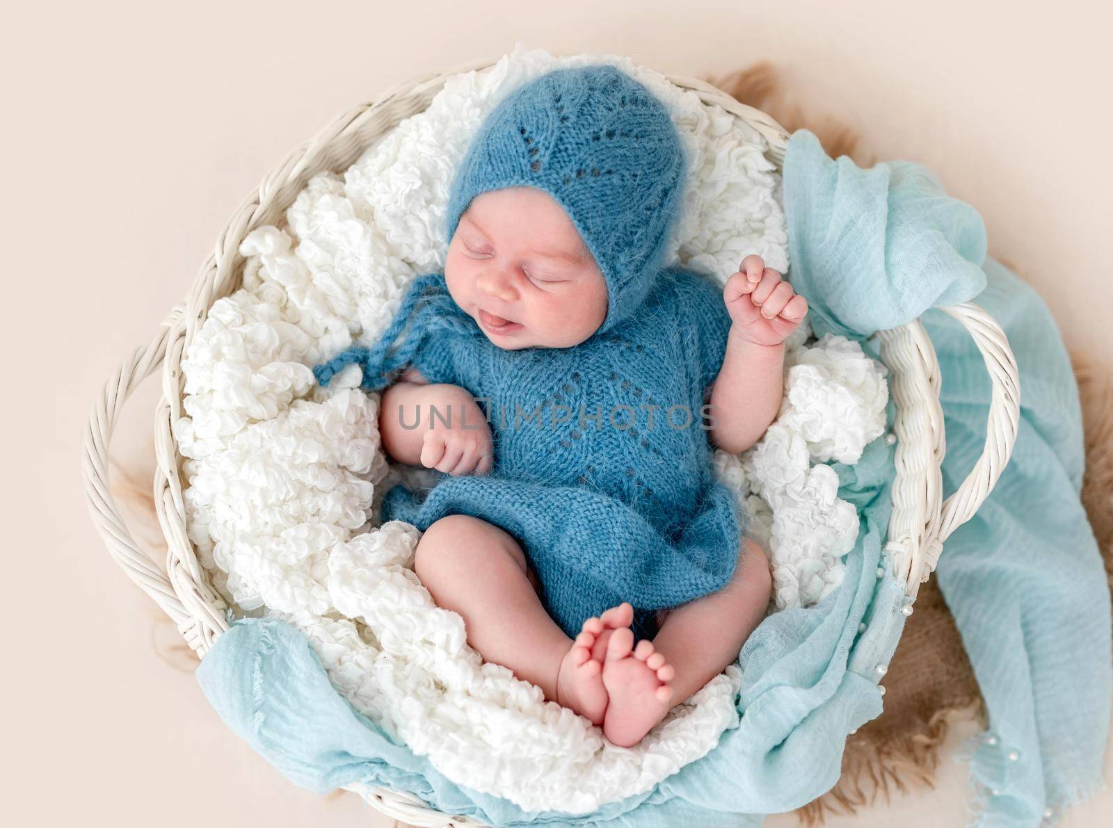 Lovely newborn with tongue out in knitted suit lying in basket