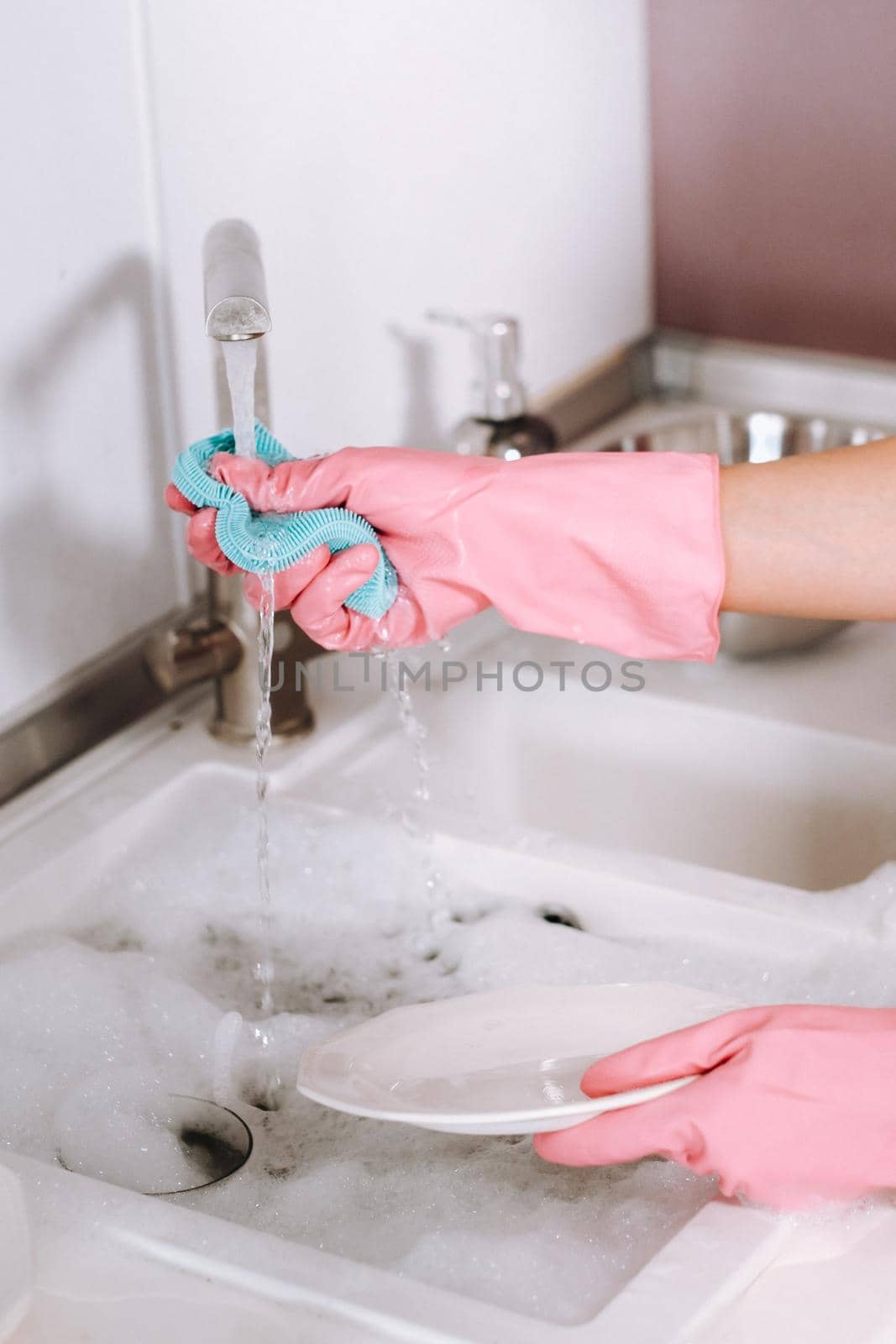 housewife girl in pink gloves washes dishes by hand in the sink with detergent. The girl cleans the house and washes dishes in gloves at home