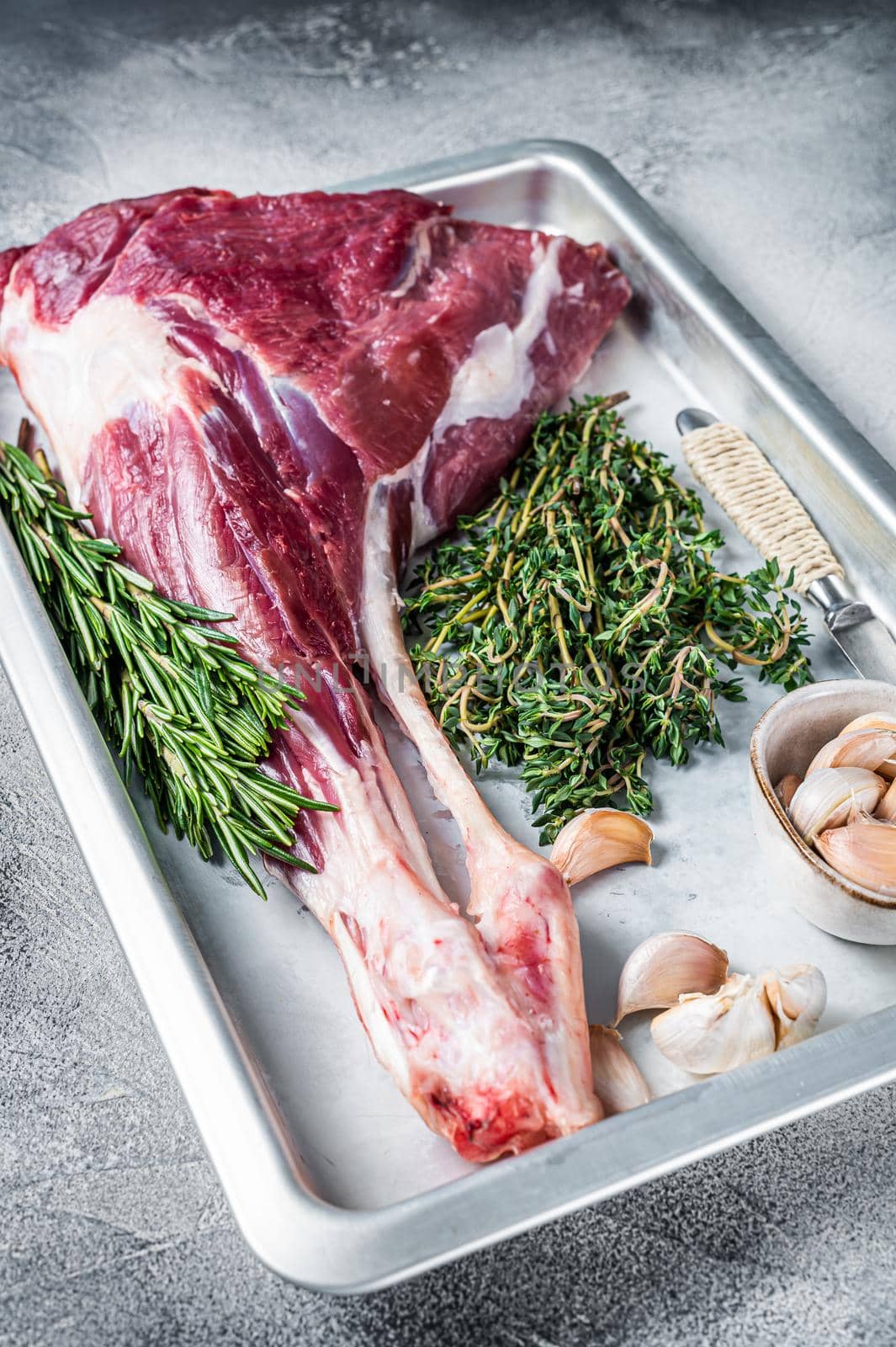 Uncooked Raw goat or lamb leg with herbs in baking tray. White background. Top view.