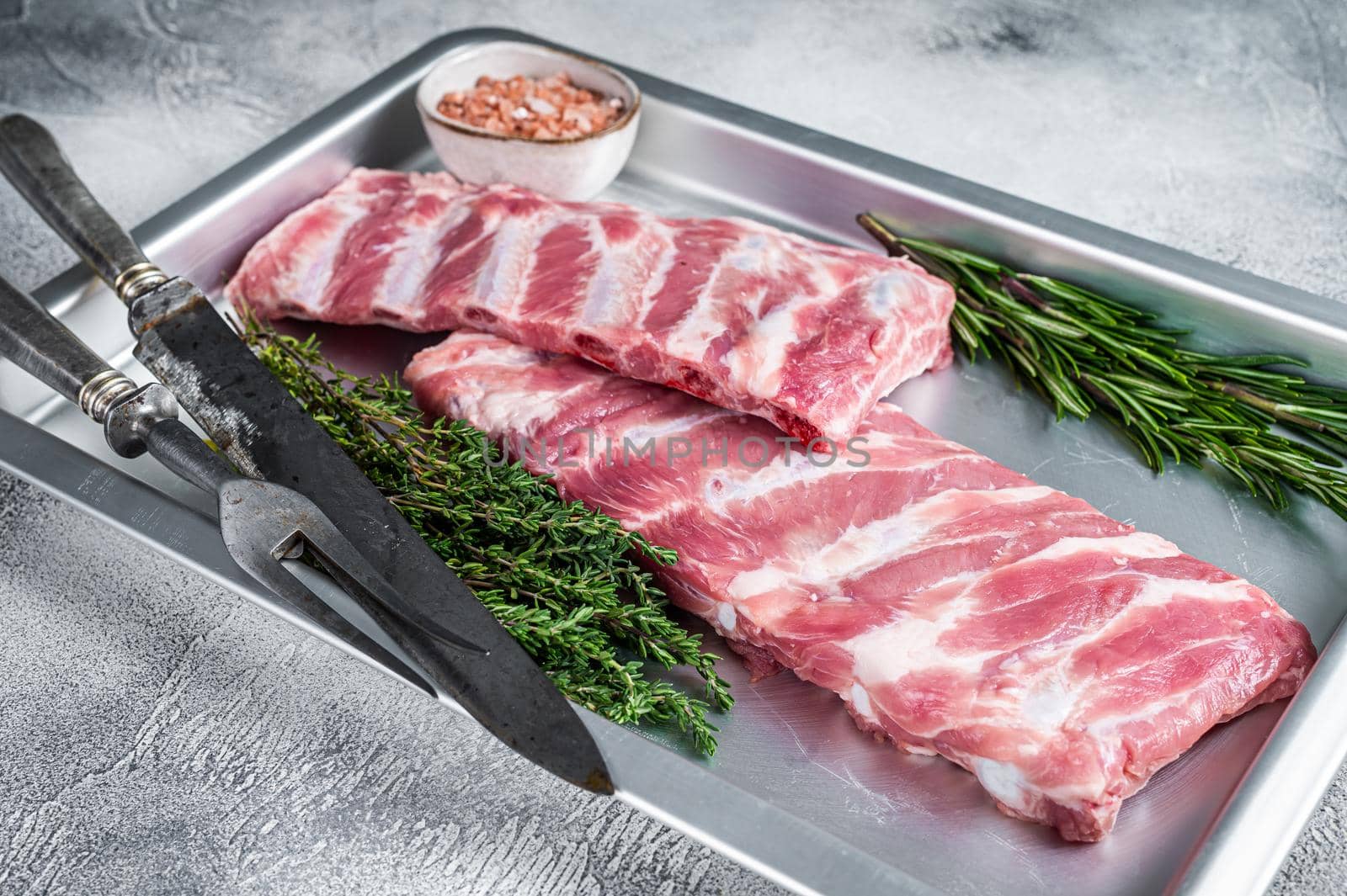 Rack of Raw pork spare ribs in kitchen oven tray with herbs. White background. Top view by Composter