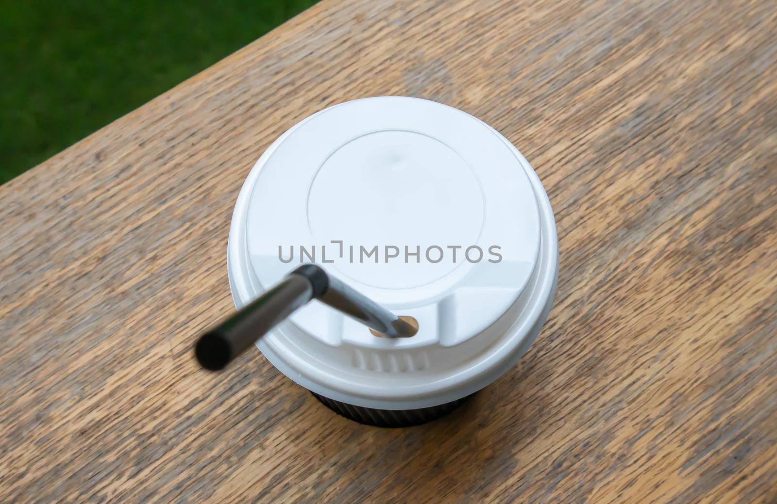One black paper coffee cup with lid outdoors in summer in sunny weather on a wooden table of a cafe, coffee shop or restaurant