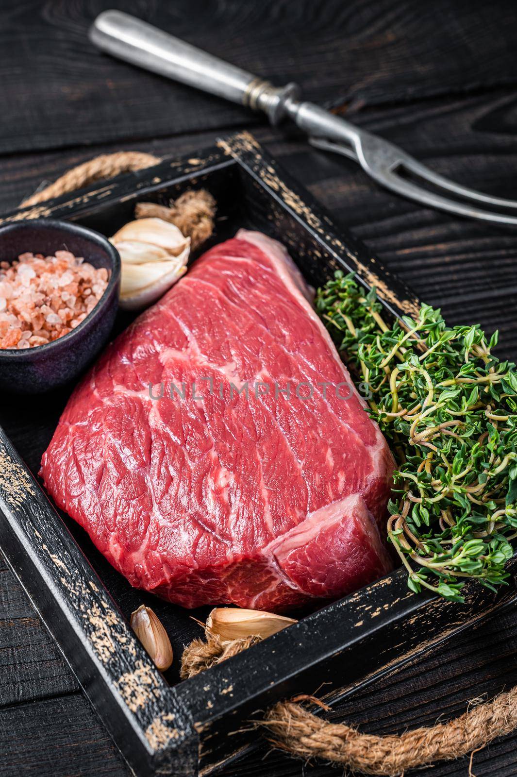 Raw top sirloin cap beef cut meat steak or Picanha in wooden tray with herbs. Black wooden background. Top view.