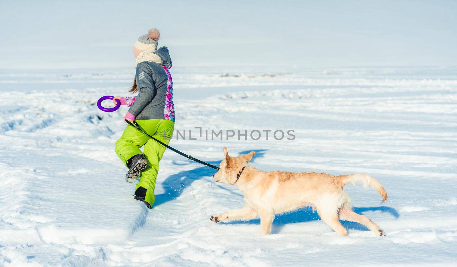 Back view of girl running in snow with dog