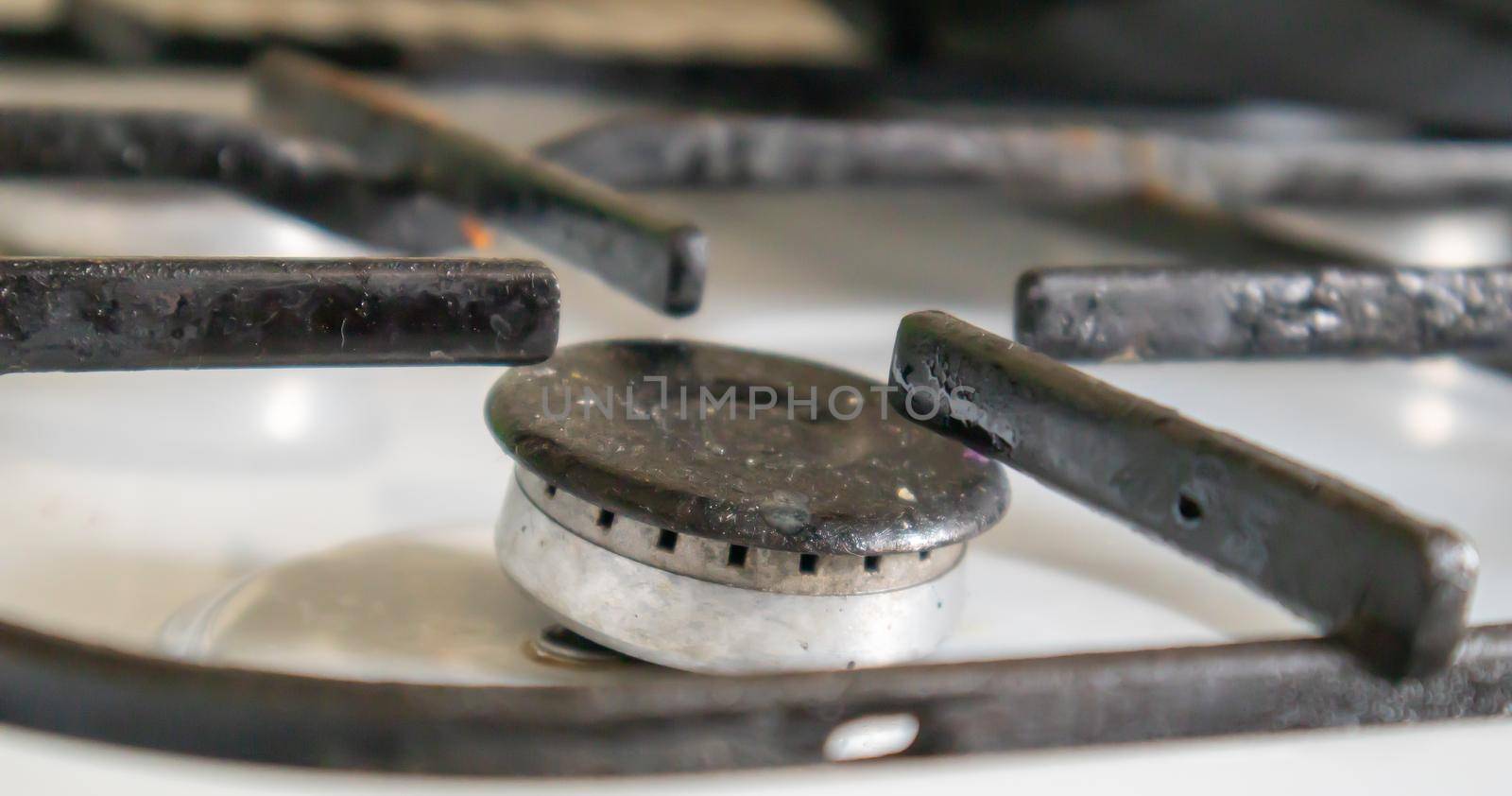 Dirty gas stove in the kitchen for cooking with vegetable oil stains and burnt food debris on the surface, close-up. Selective focus. Grease-covered gas hob in the kitchen