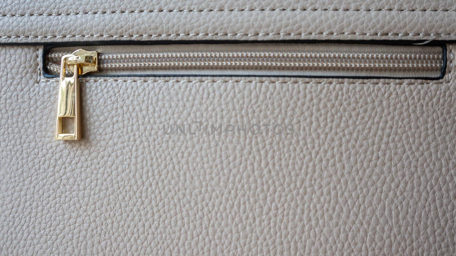 Natural or artificial leather texture. Fragment of a beige or powdery bag with a zipper and stitching. Zipper or clasp bag design element. Bovine skin texture with snake. Macro photo, selective focus