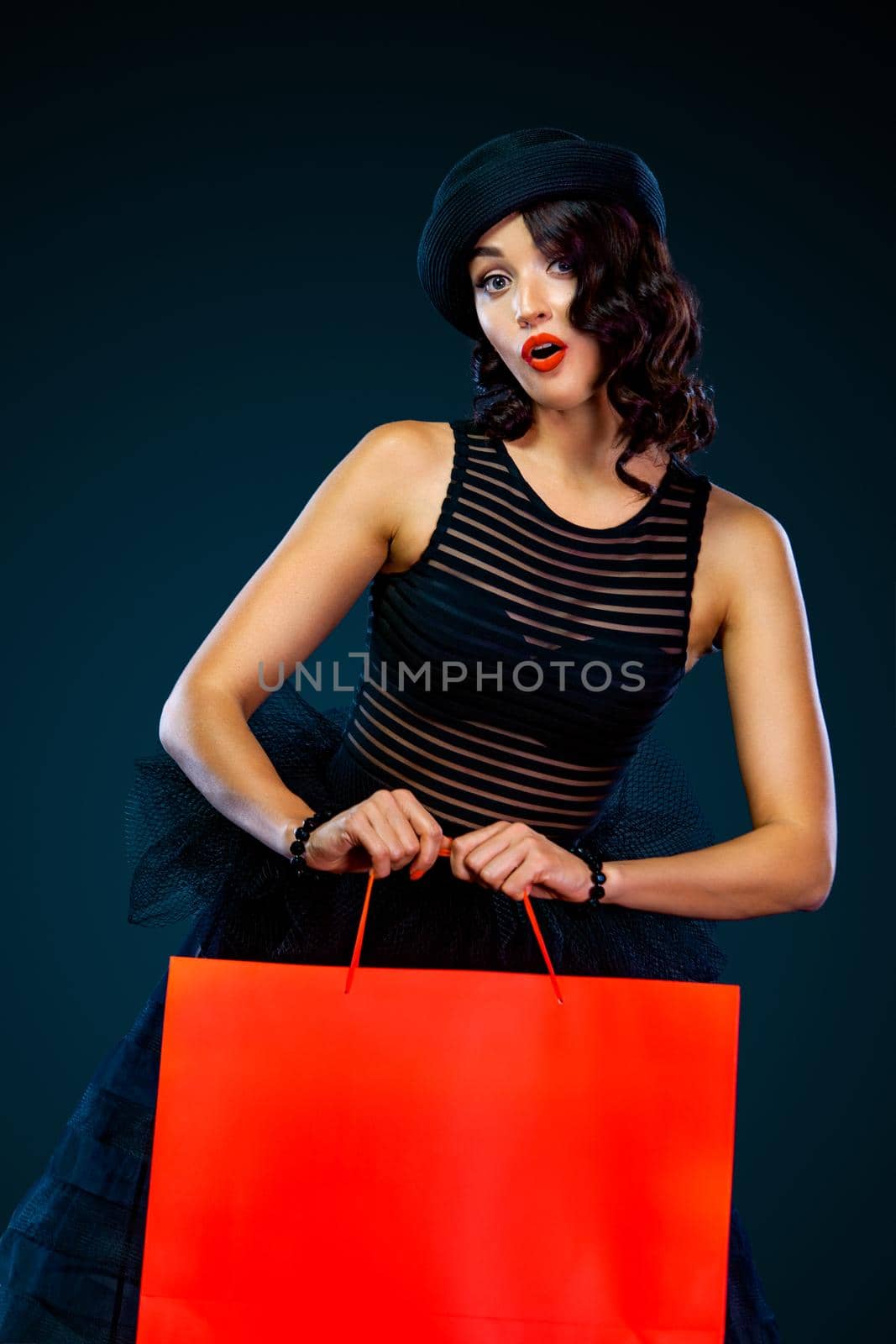 Black friday sale concept for shop. Shopping woman in dress and hat holding red bag isolated on dark background by MikeOrlov