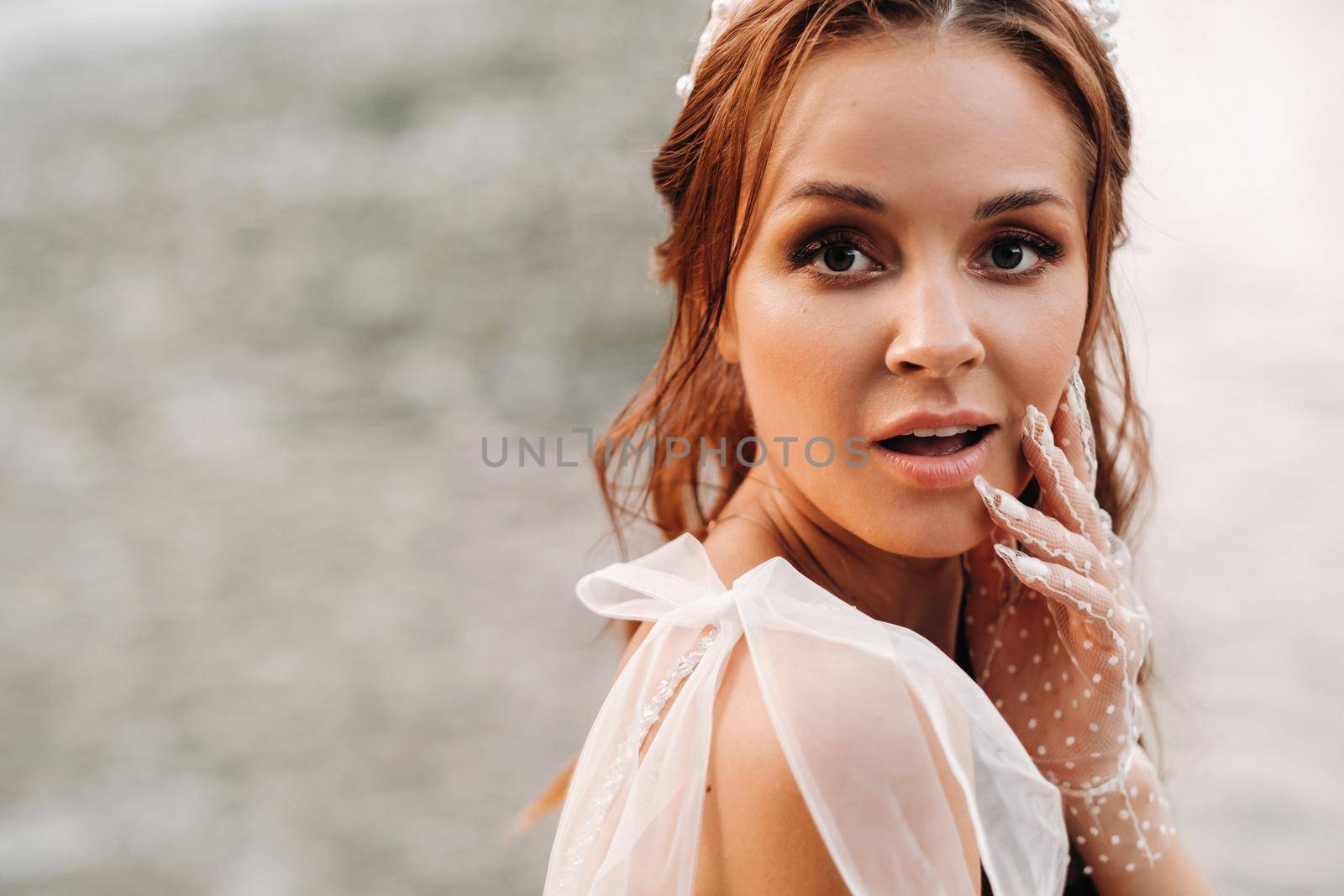 An elegant bride in a white dress, gloves and bare feet is sitting near a waterfall in the Park enjoying nature.A model in a wedding dress and gloves at a nature Park.Belarus by Lobachad