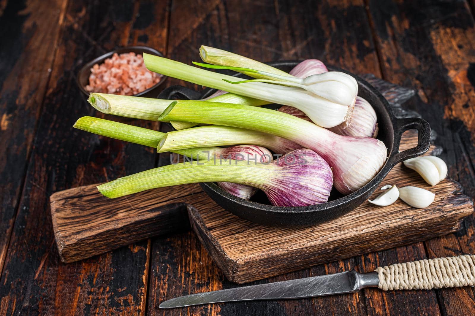 Young Spring garlic bulbs and cloves in a pan. Dark Wooden background. Top view.