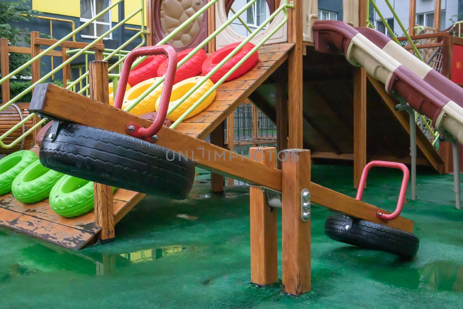 A courtyard of high-rise buildings with a modern and large playground made of wood and plastic on a rainy summer day without people. Empty outdoor playground. A place for children's games and sports