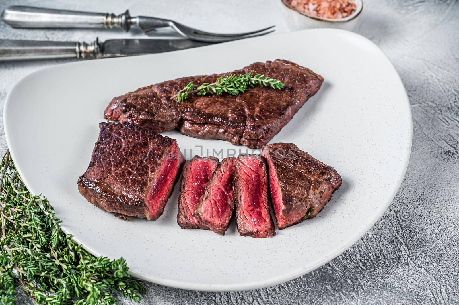 Roasted sliced rump beef meat steak on a plate with thyme. White background. Top view by Composter