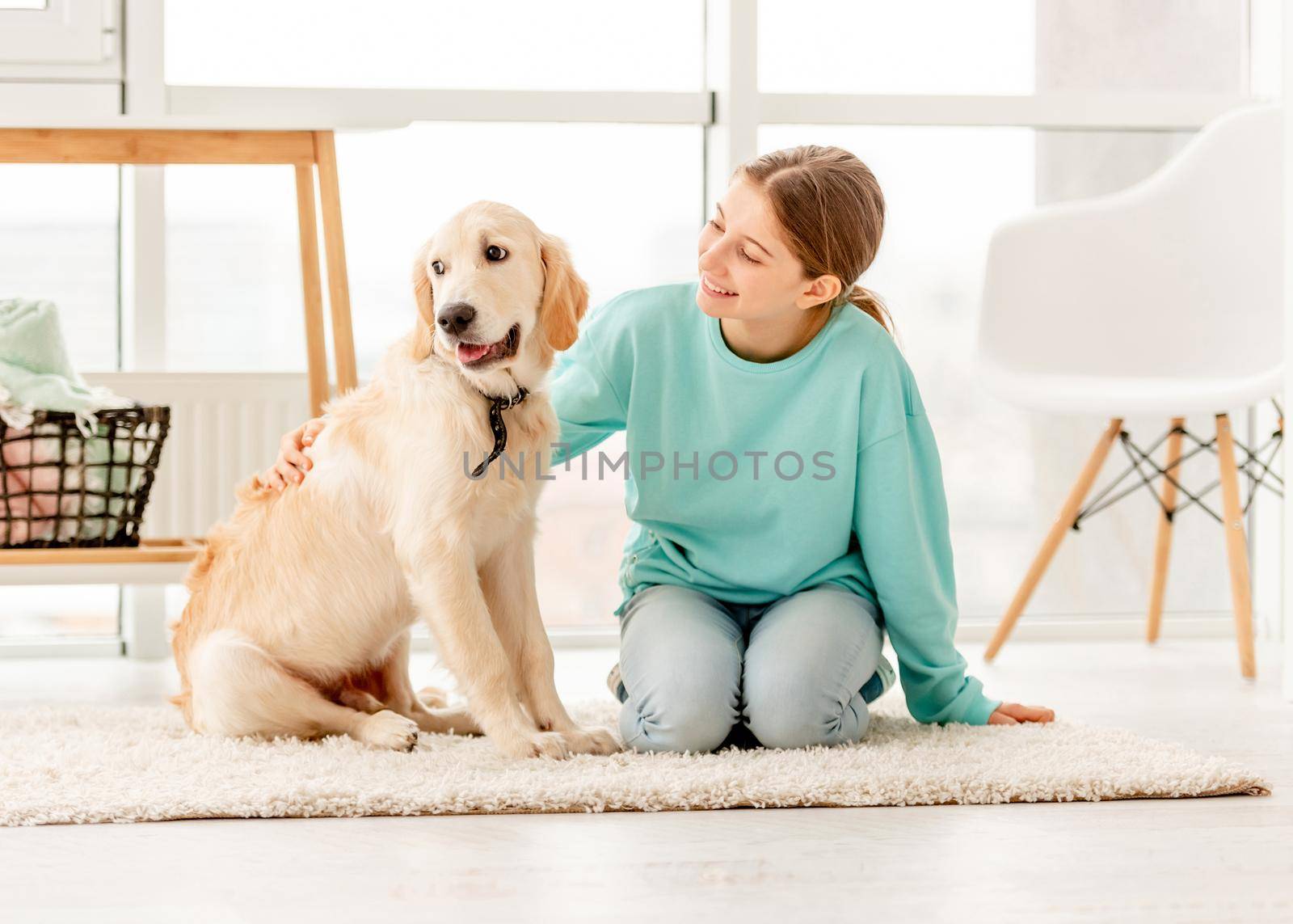 Smiling girl with lovely young dog sitting on floor in light room