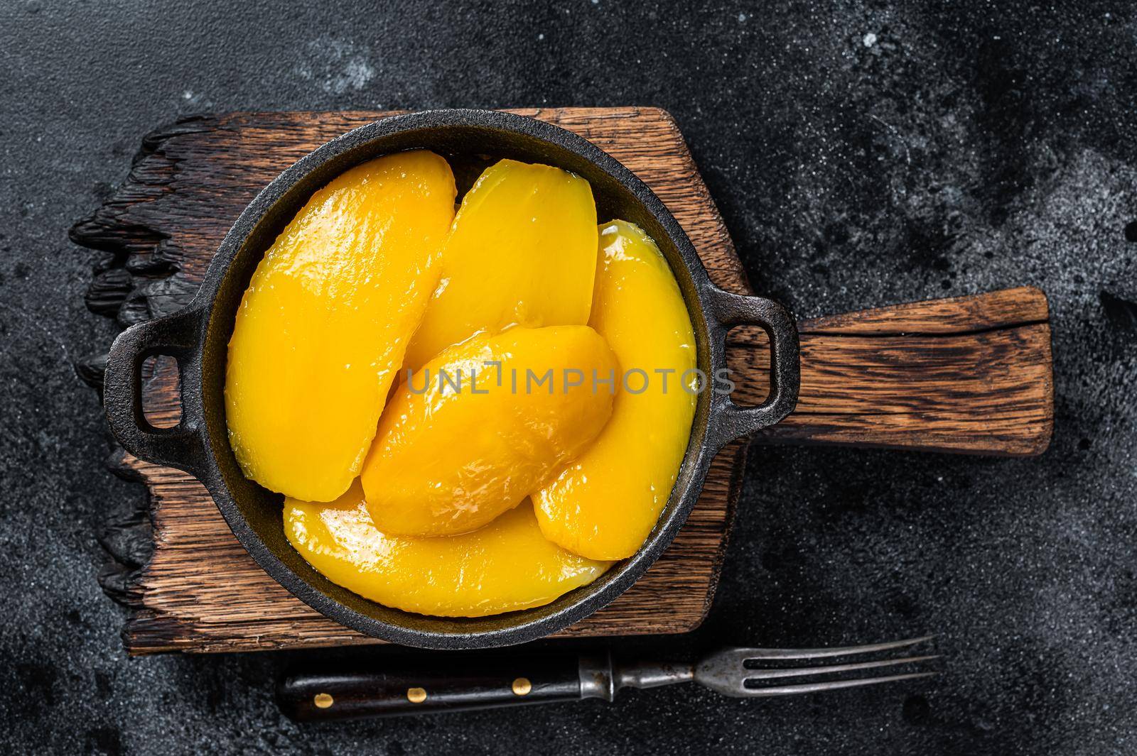 Canned mango slices in bowl. Black background. Top view.