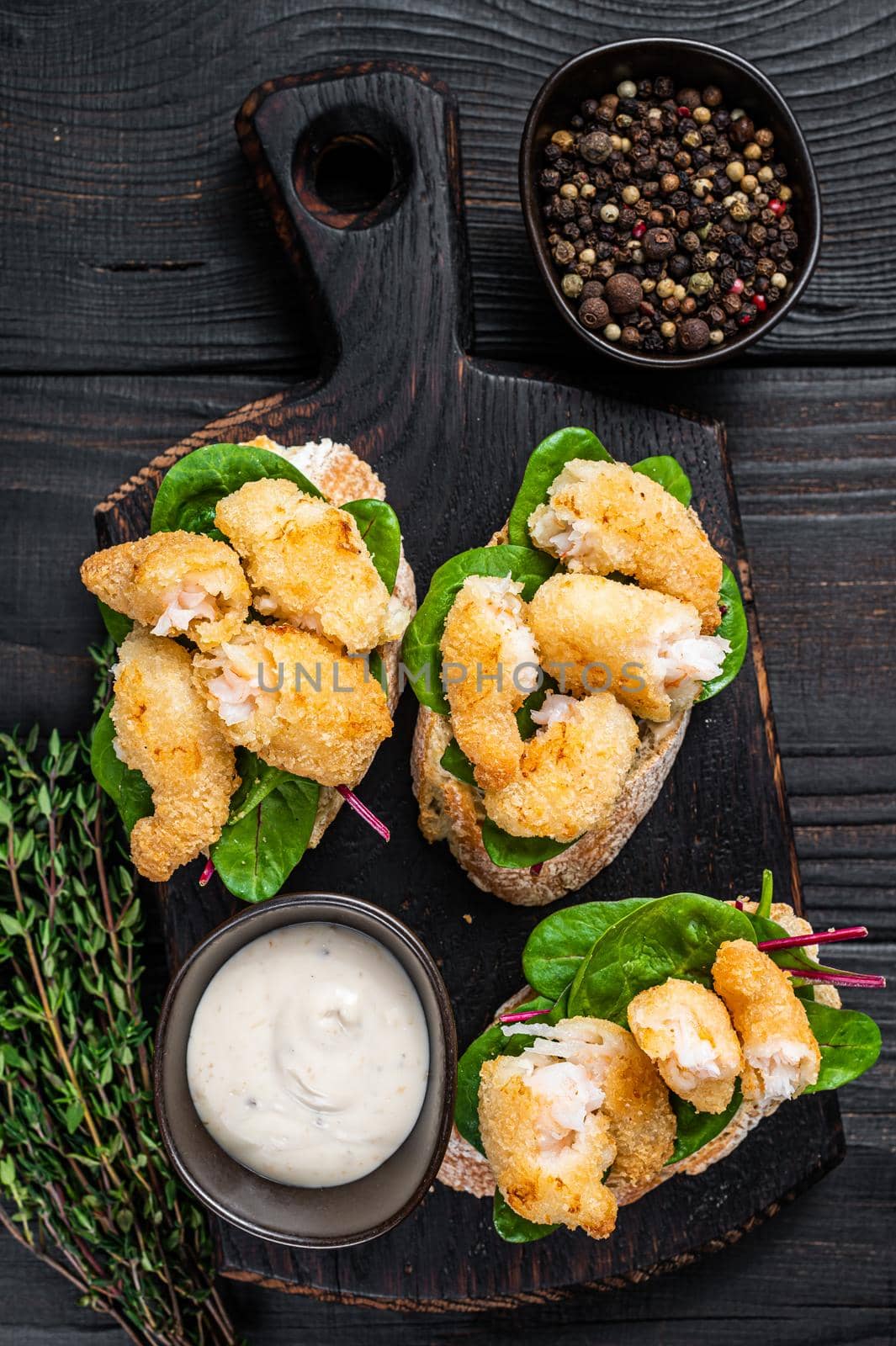 Toasts with Crispy Fried Shrimps Prawns and green salad on a wooden board. Black wooden background. Top view.