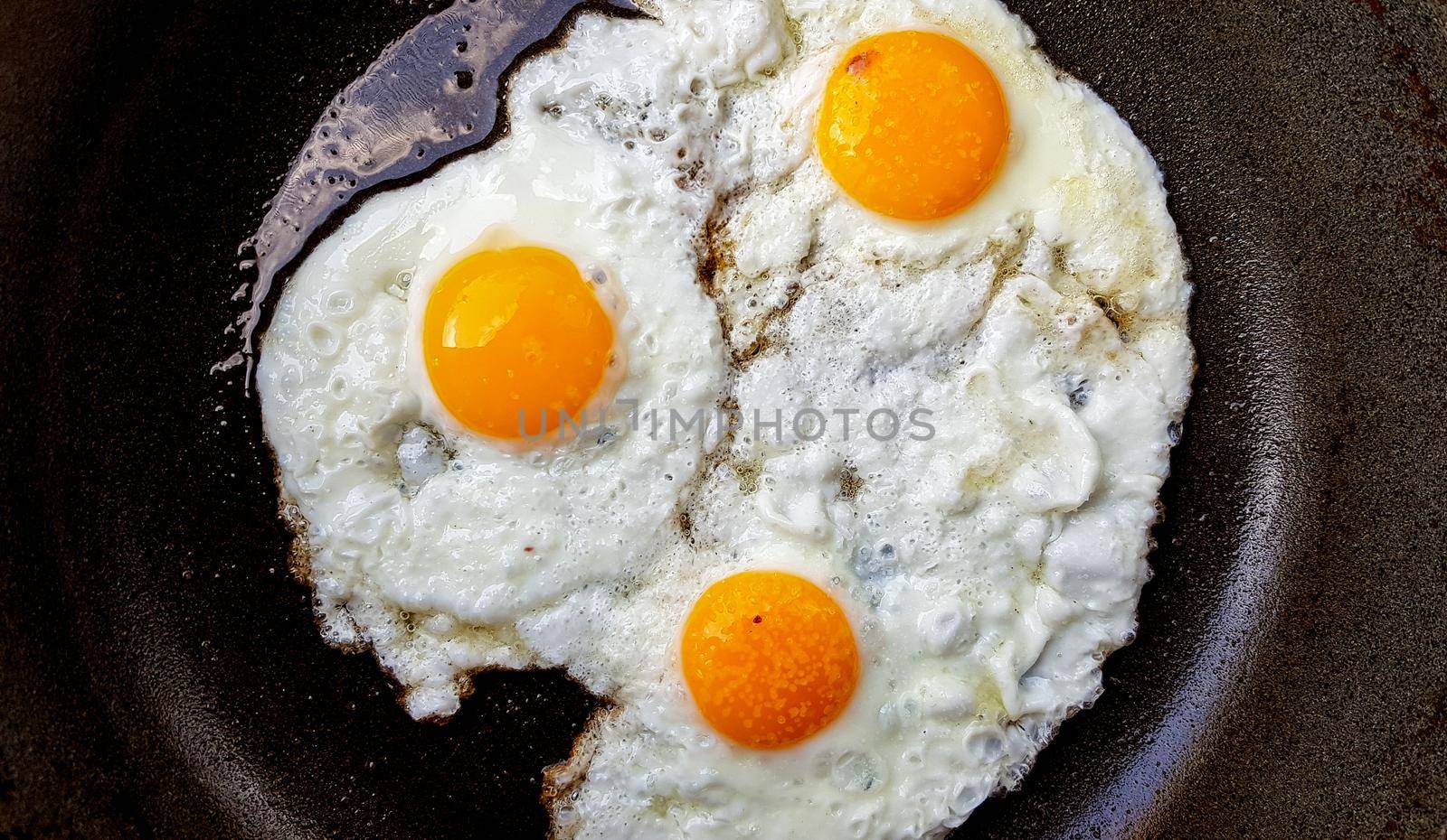 Three free range fried eggs in a hot non stick frying pan.
