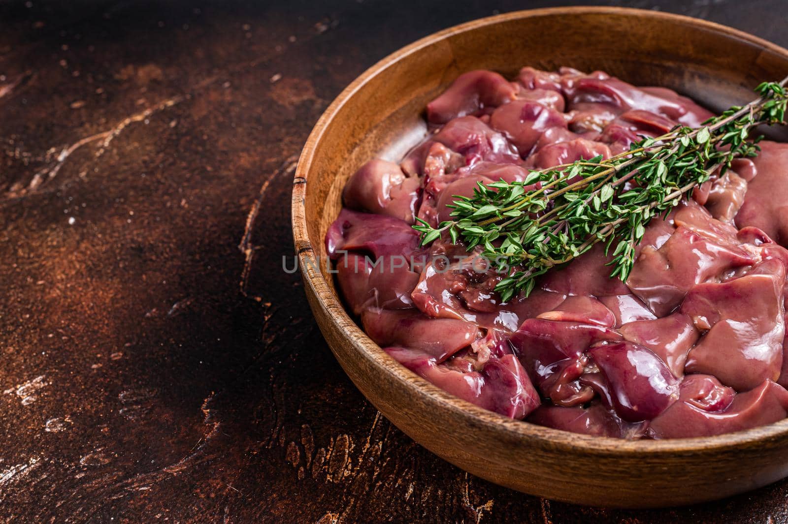 Raw chicken liver offals in a wooden plate. Dark background. Top view. Copy space.