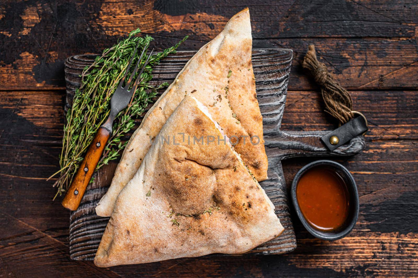 Homemade Calzone closed pizza with ham and cheese on wooden board. Dark wooden background. Top view.