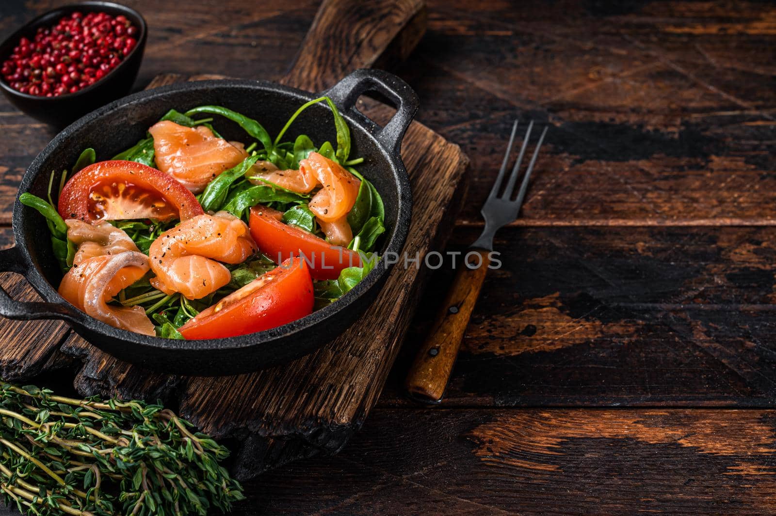 Fresh salmon salad with arugula, tomato and green vegetables. Dark wooden background. Top View. Copy space by Composter