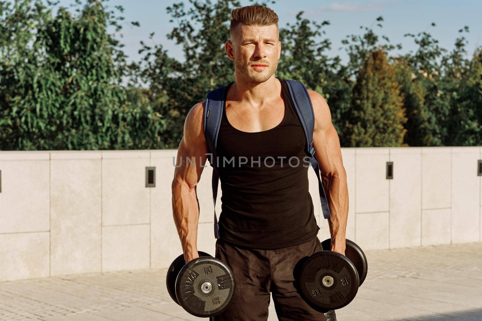 athletic man in black t-shirt with dumbbells in the park training. High quality photo