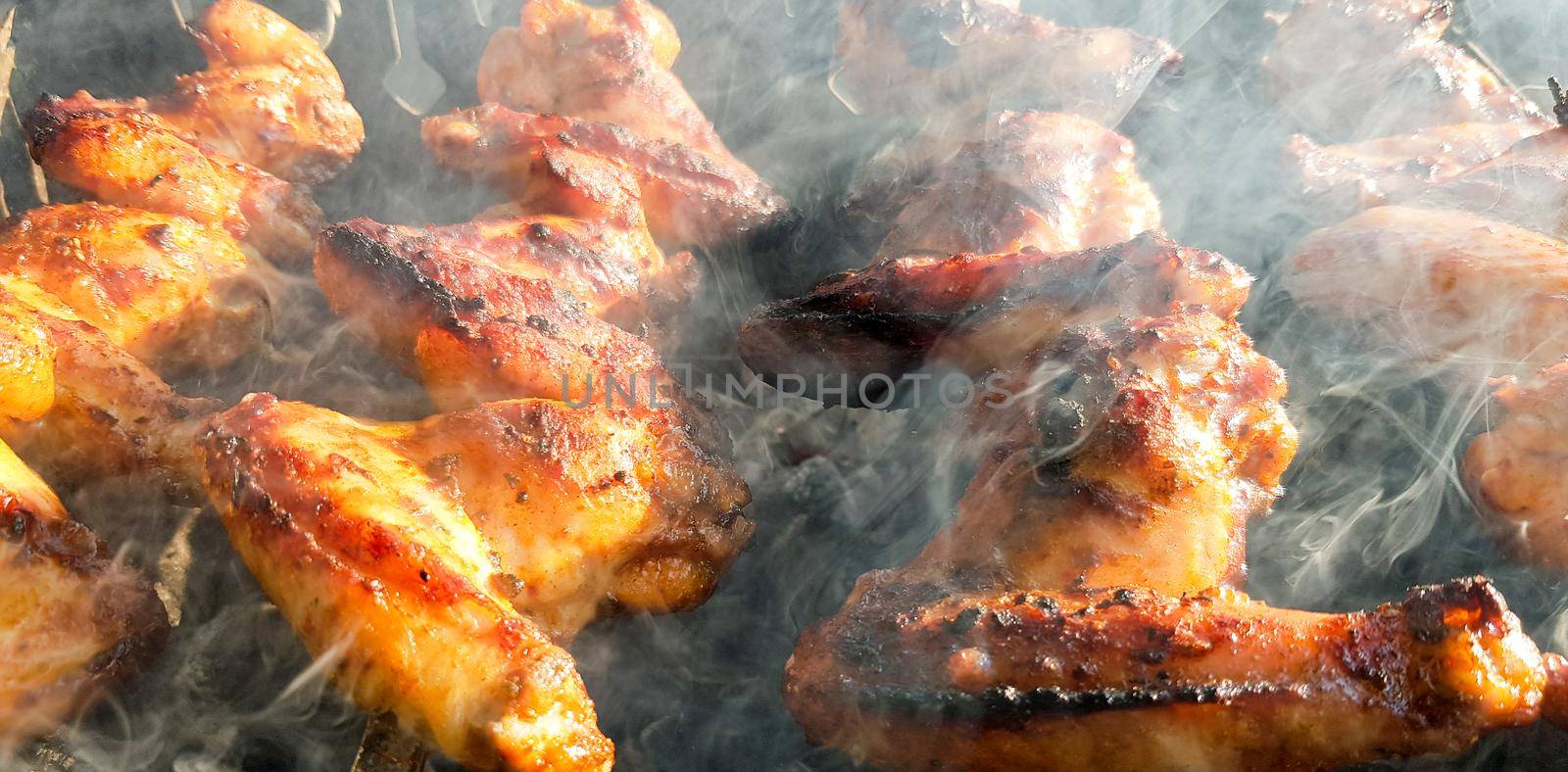 Delicious juicy grilled chicken wings outdoors in smoke. BBQ Chicken Cooking Process.