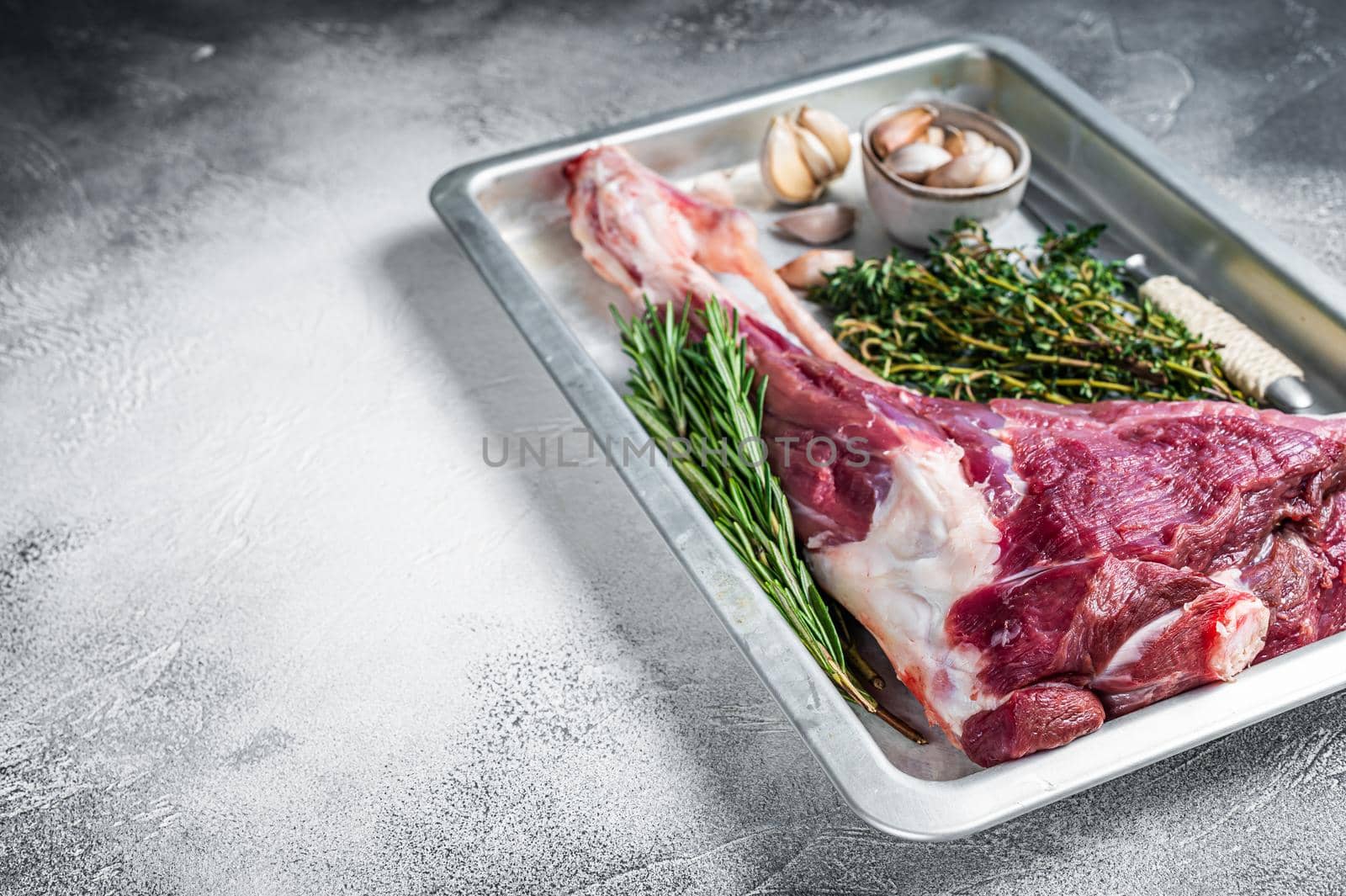 Uncooked Raw goat or lamb leg with herbs in baking tray. White background. Top view. Copy space by Composter