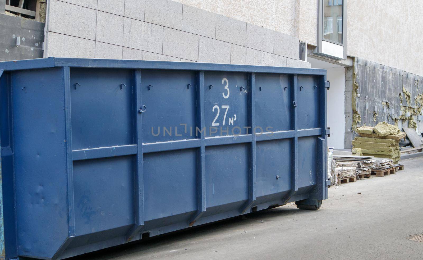 Metal durable blue industrial trash bin for outdoor trash at construction site. Large waste basket for household or industrial waste. A pile of waste