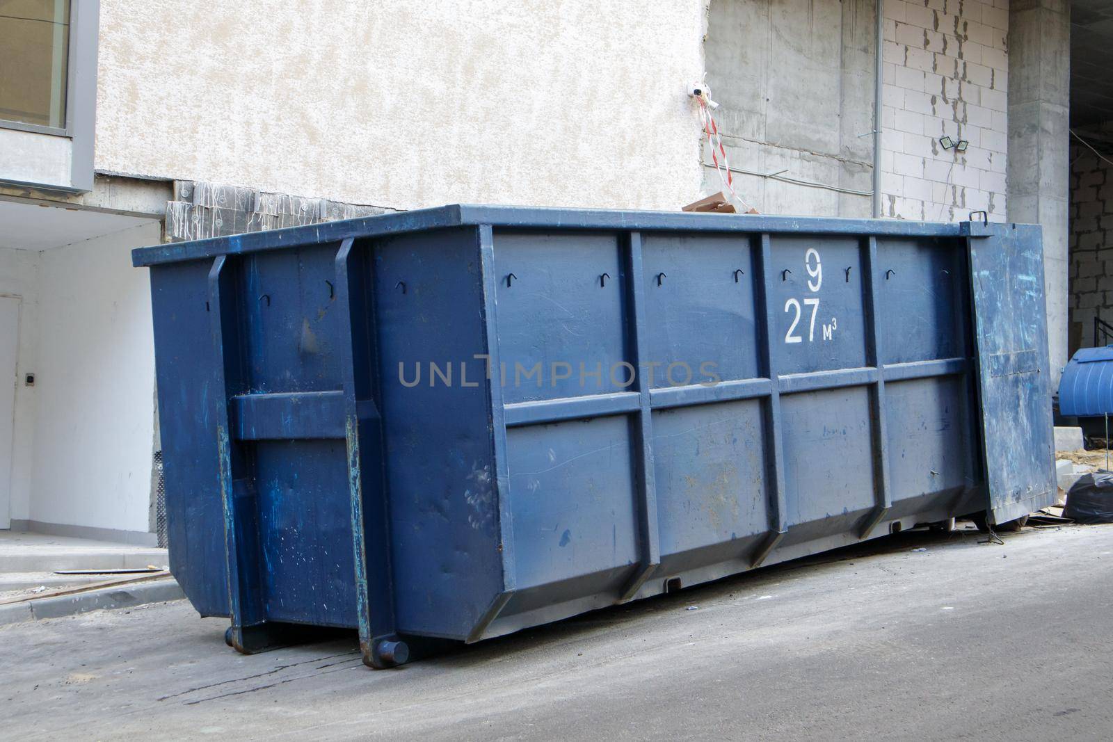 Metal durable blue industrial trash bin for outdoor trash at construction site. Large waste basket for household or industrial waste. A pile of waste