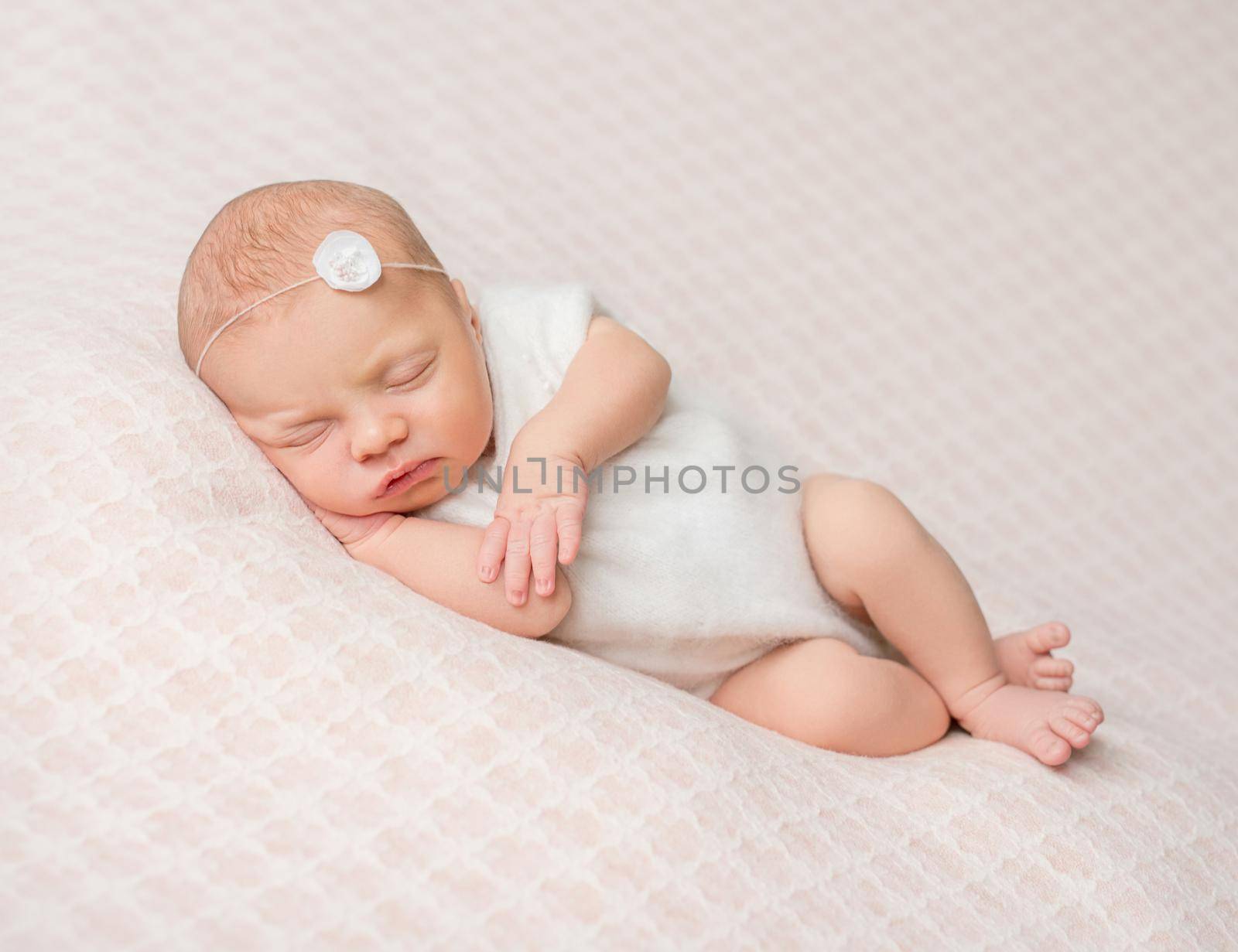sweet sleeping newborn girl with flower on her headband in white suit