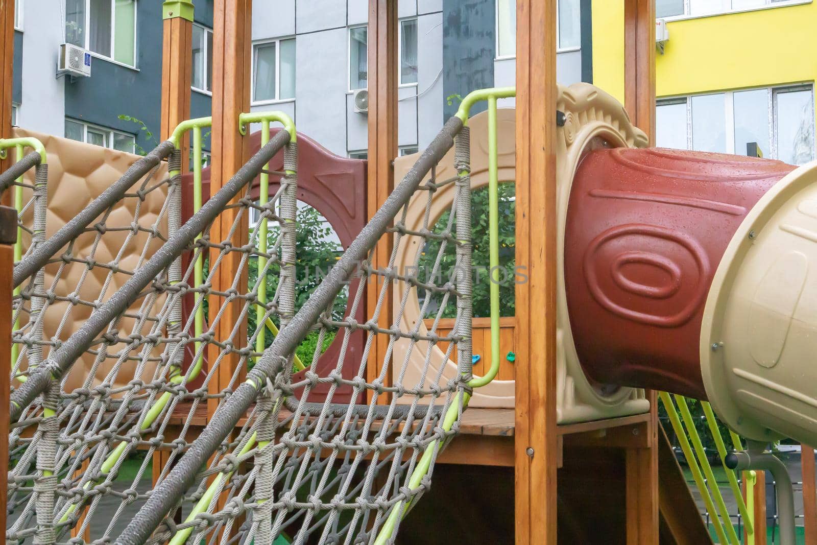 A courtyard of high-rise buildings with a modern and large playground made of wood and plastic on a rainy summer day without people. Empty outdoor playground. A place for children's games and sports