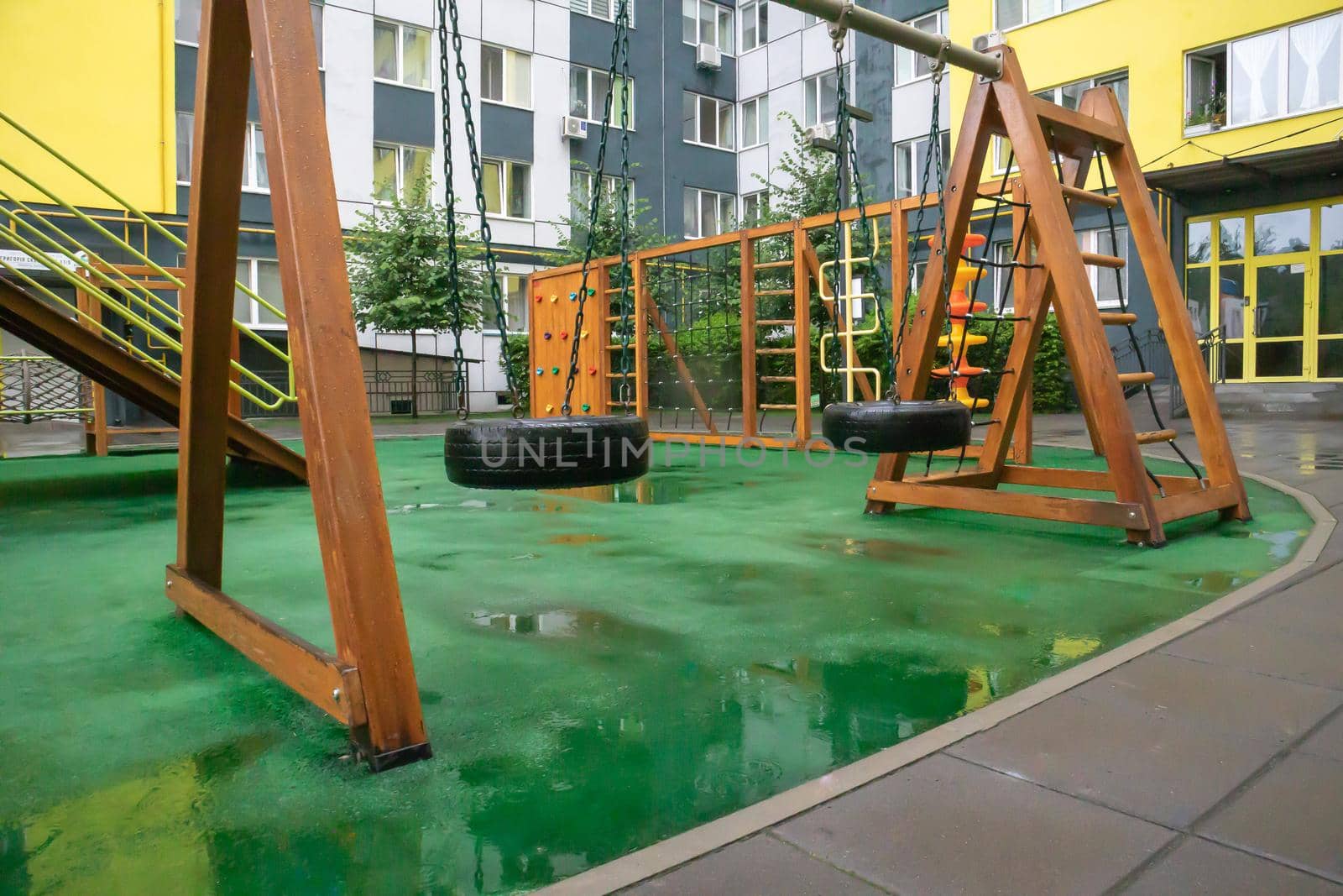 The courtyard of a high-rise building with a modern large playground made of wood and plastic on a rainy summer day without people. Ukraine, Kiev - August 19, 2021