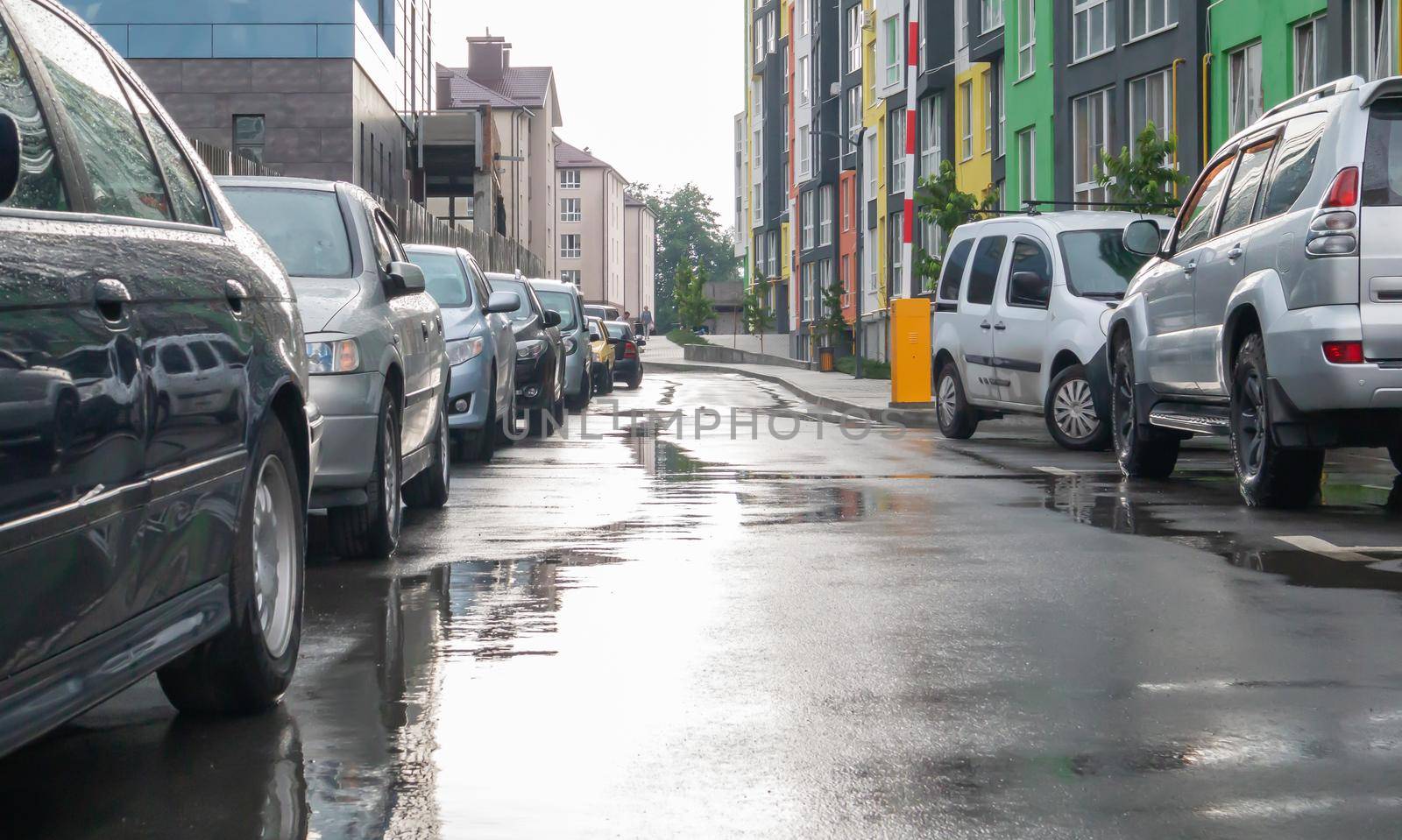 Street in a city without people with parked cars in rainy weather. Rain on the road. Rain and cars. Background of parked cars on a rainy city street. Symmetrical parked cars
