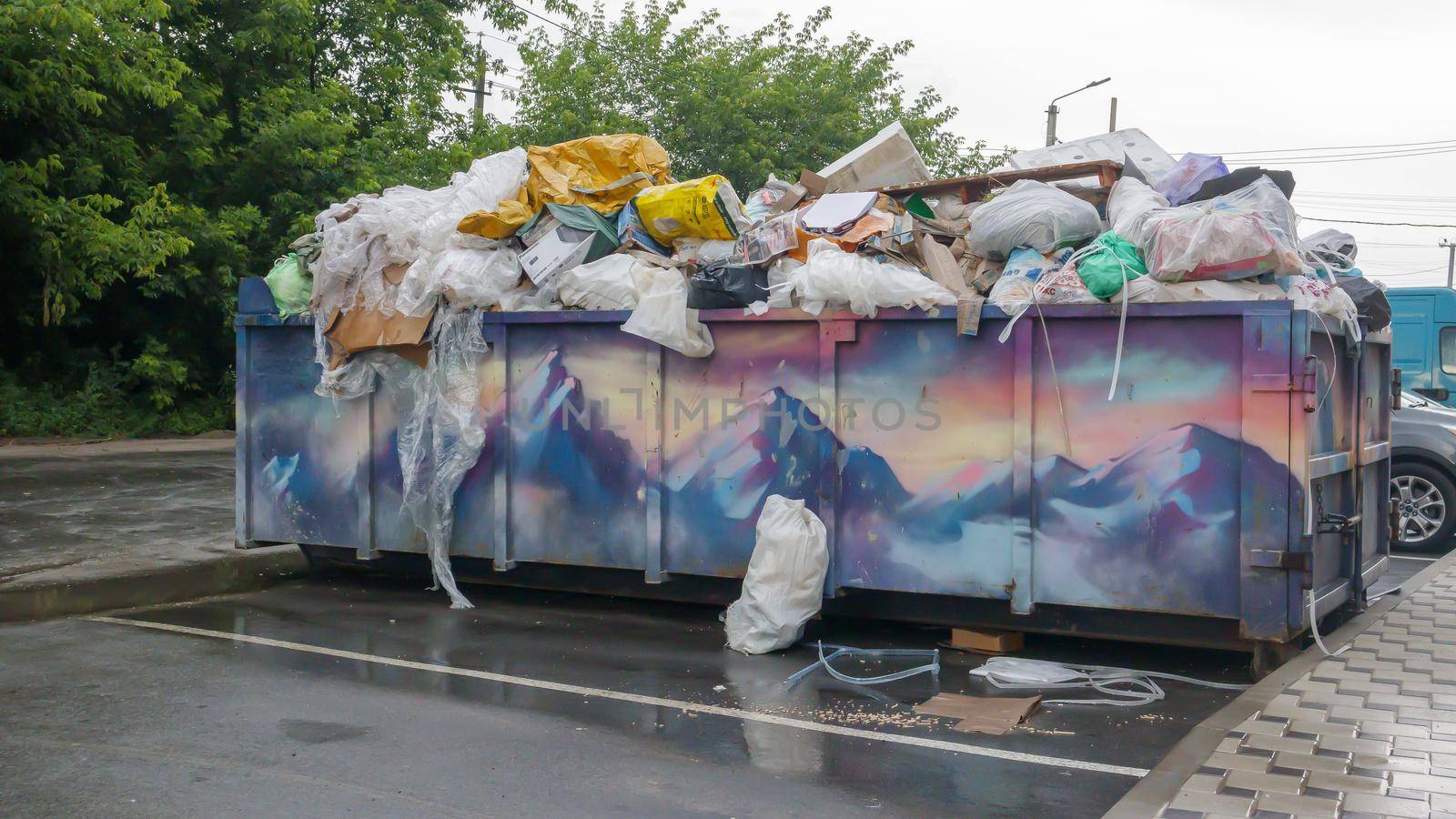 Metal durable blue industrial trash bin for outdoor trash at construction site. Large waste basket for household or industrial waste. A pile of waste. Ukraine, Kiev - August 09, 2021