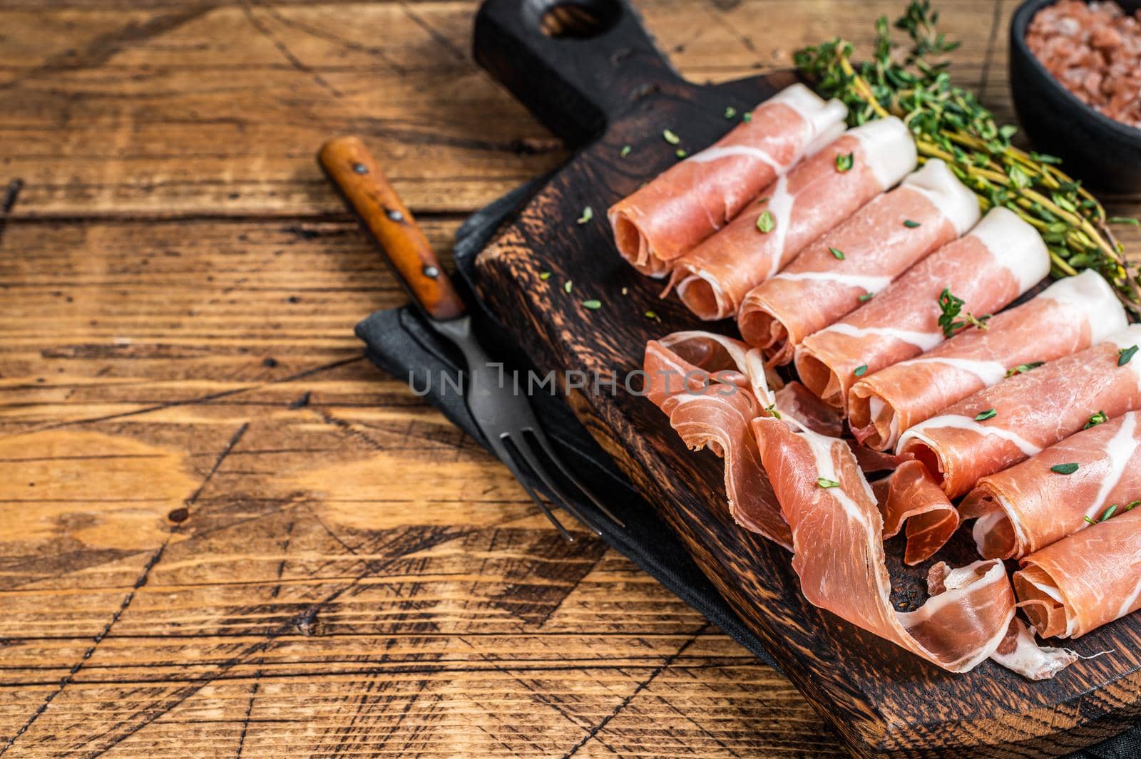 Prosciutto crudo Dry cured parma ham on a wooden cutting board with thyme. wooden background. Top View. Copy space.