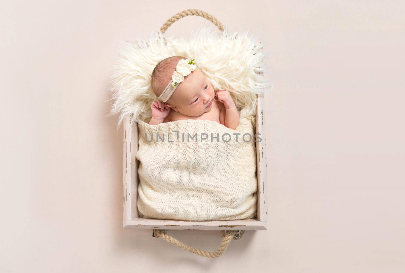 Adorable child wearing hairband laying in a baby basket with her eyes opened widely, closeup