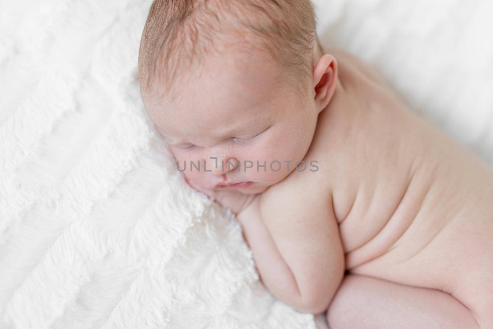 Adorable hairy naked infant sleeping on his belly tighly, light skin and cute position close up