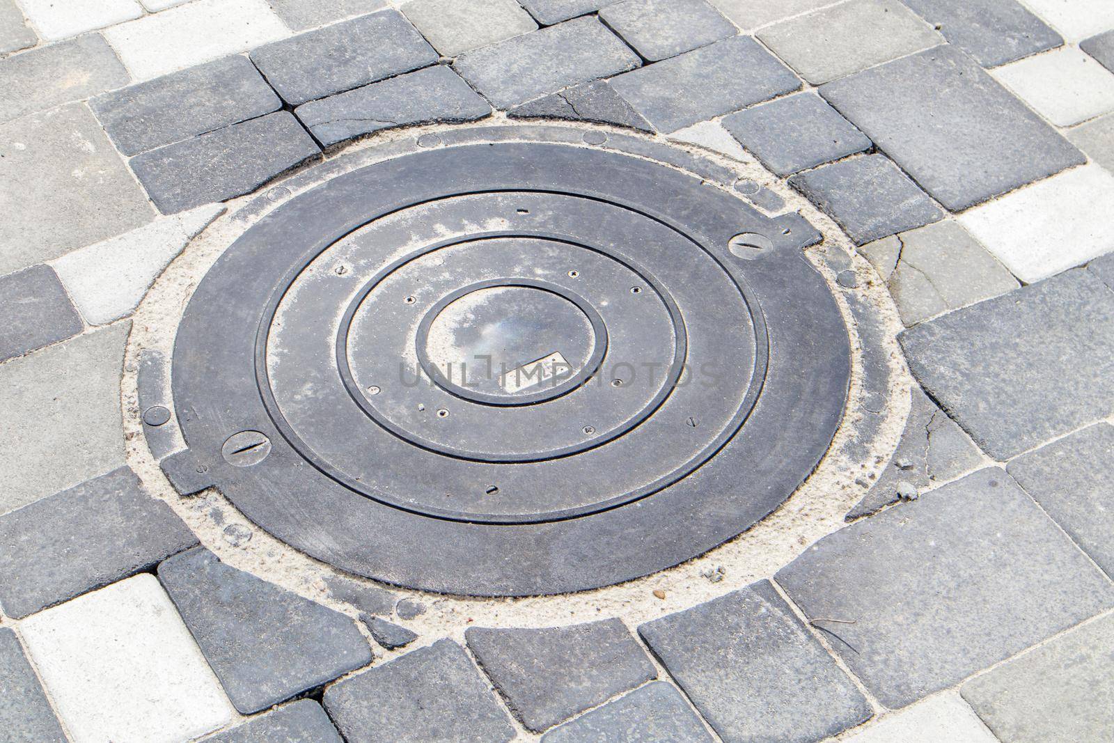 New plastic manhole cover on the sidewalk lined with gray paving slabs. The concept of sewerage, underground communications. Installation of a new sewer hatch. Construction industry