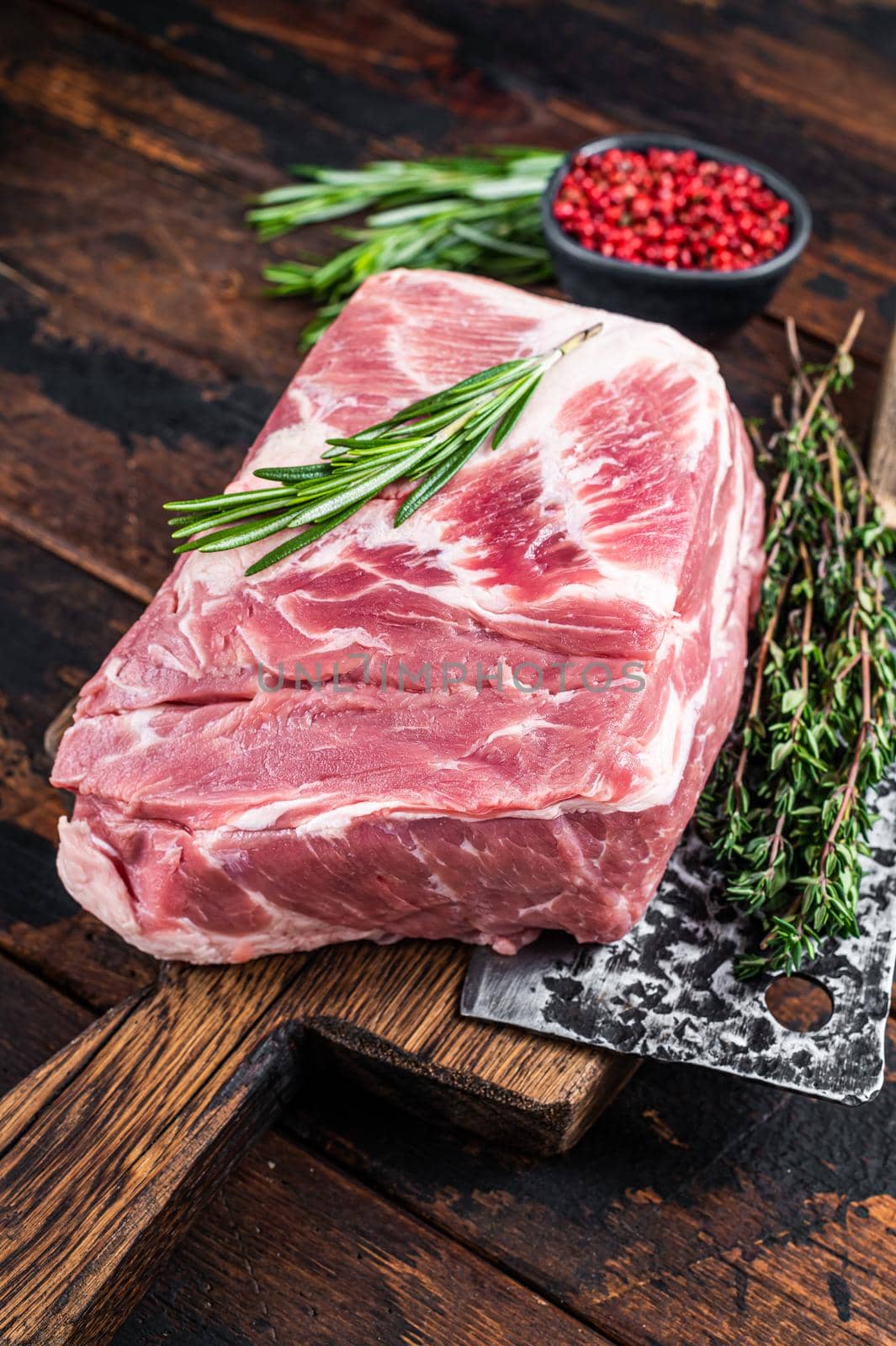 Pork neck raw meat for fresh Chop steaks on wooden cutting board with butcher cleaver. Dark wooden background. Top view.