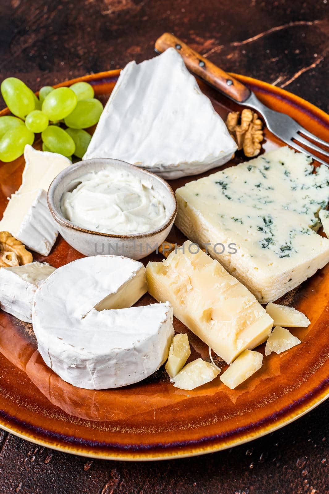 Cheese plate with Brie, Camembert, Roquefort, blue cream cheese, grape and nuts. Dark background. Top view by Composter