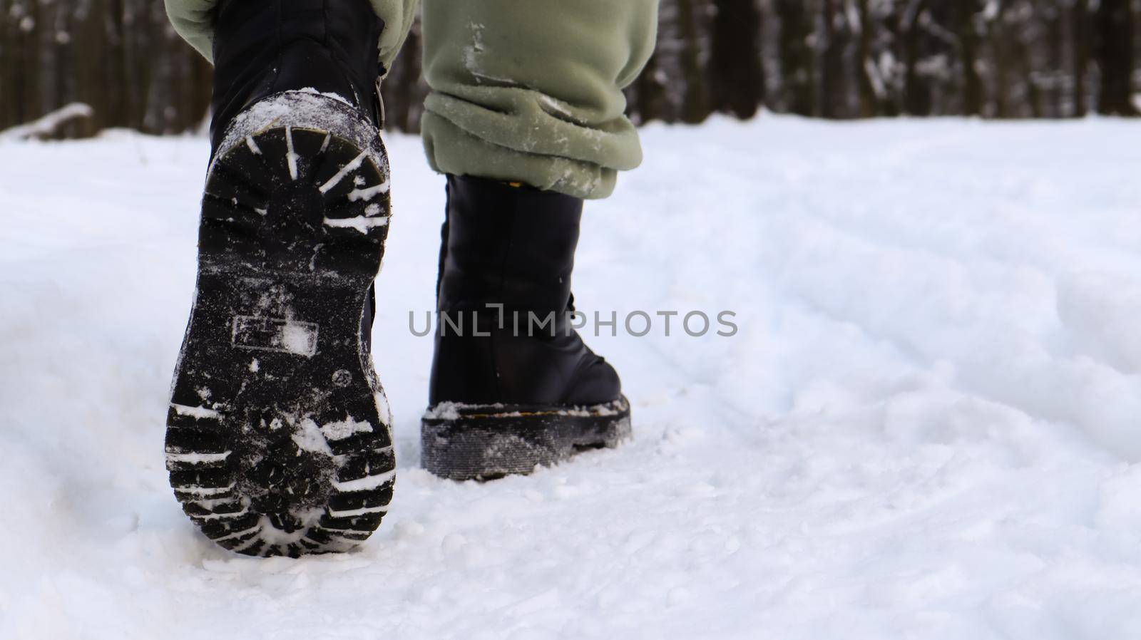 Female legs in black boots, winter walk in the snow. Active woman walking away from the camera in the winter forest. Focus on your legs. Beautiful white winter weather with fresh snowfall