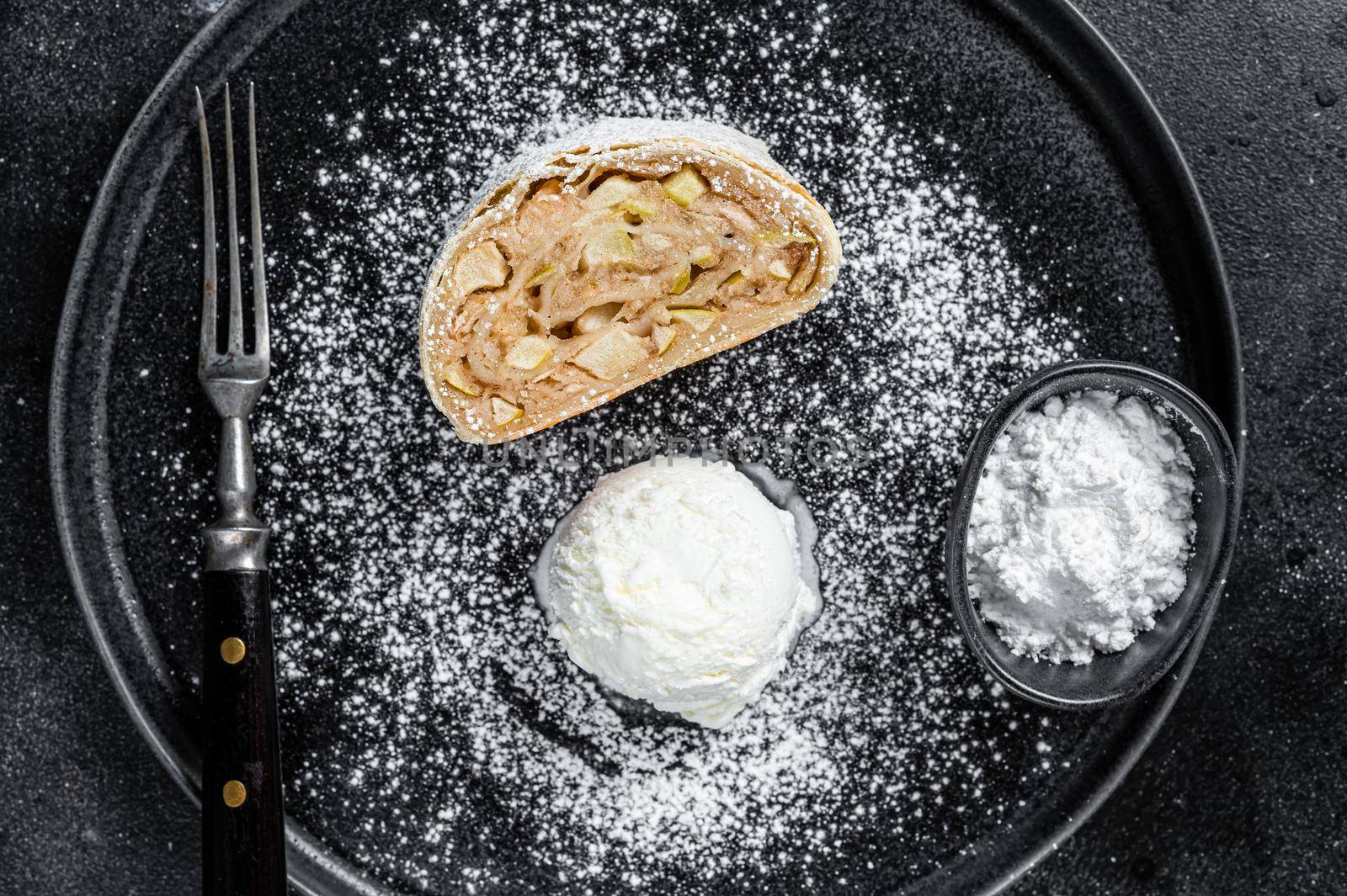 Apple strudel with cinnamon, powdered sugar and vanilla ice cream on a plate. Black background. Top view by Composter